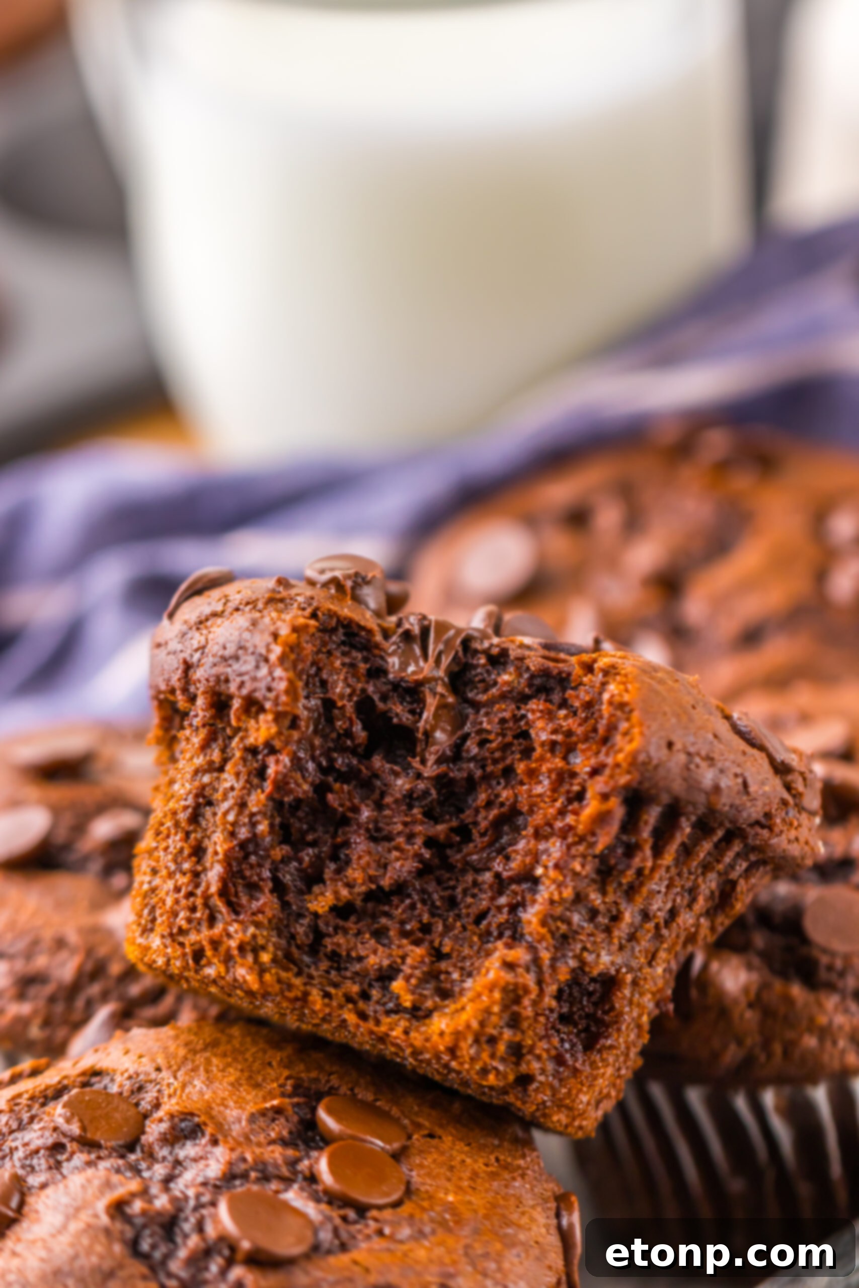 Costco Double Chocolate Muffins Bakery Style Jumbo Rich Moist 2 A freshly baked Costco Double Chocolate Muffin with a bite taken out, resting on a rustic surface.