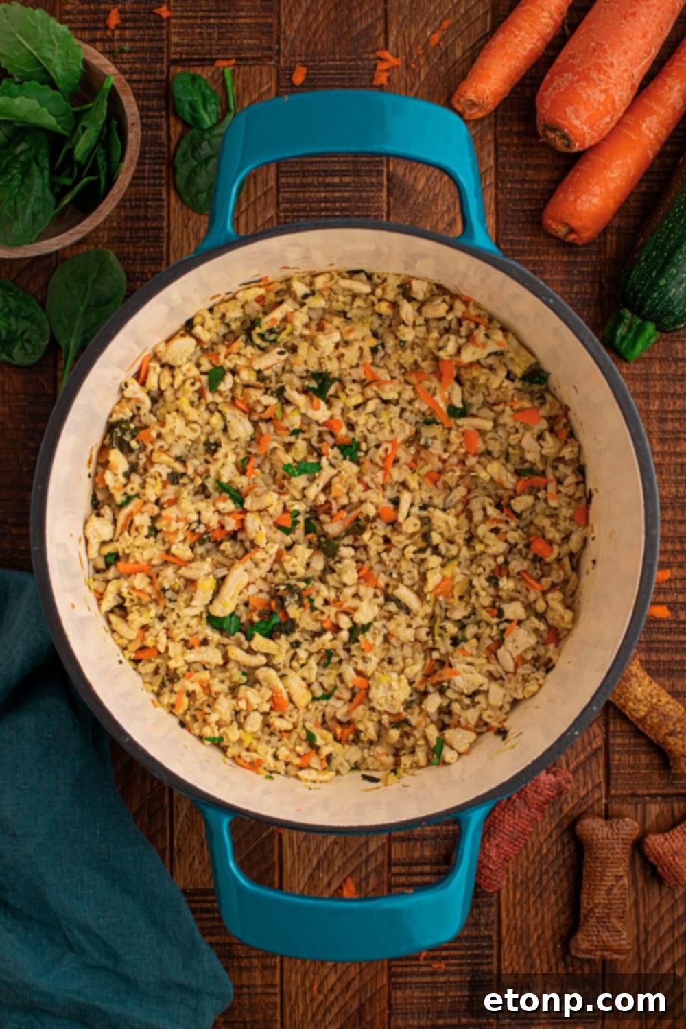 overhead look of Homemade Turkey and Rice Dog Food with Veggies in a blue pot with fresh herbs and whole carrots behind the pot on table 