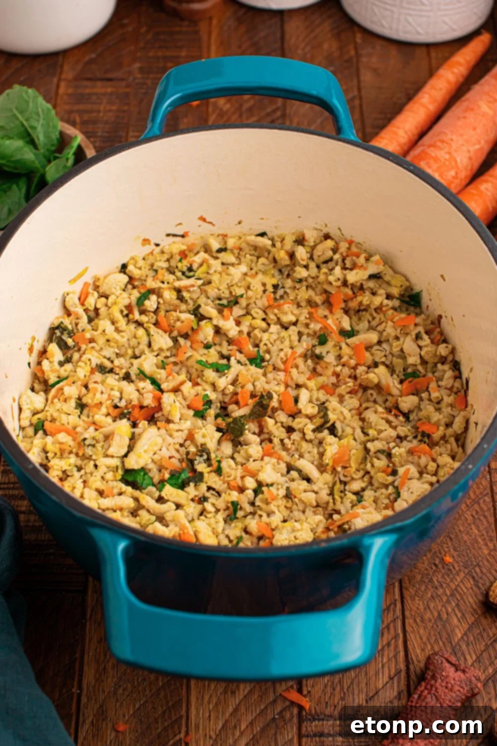 Homemade Turkey and Rice Dog Food with Veggies in a pot sitting on table with fresh herbs, carrots, and white containers behind pan on table 