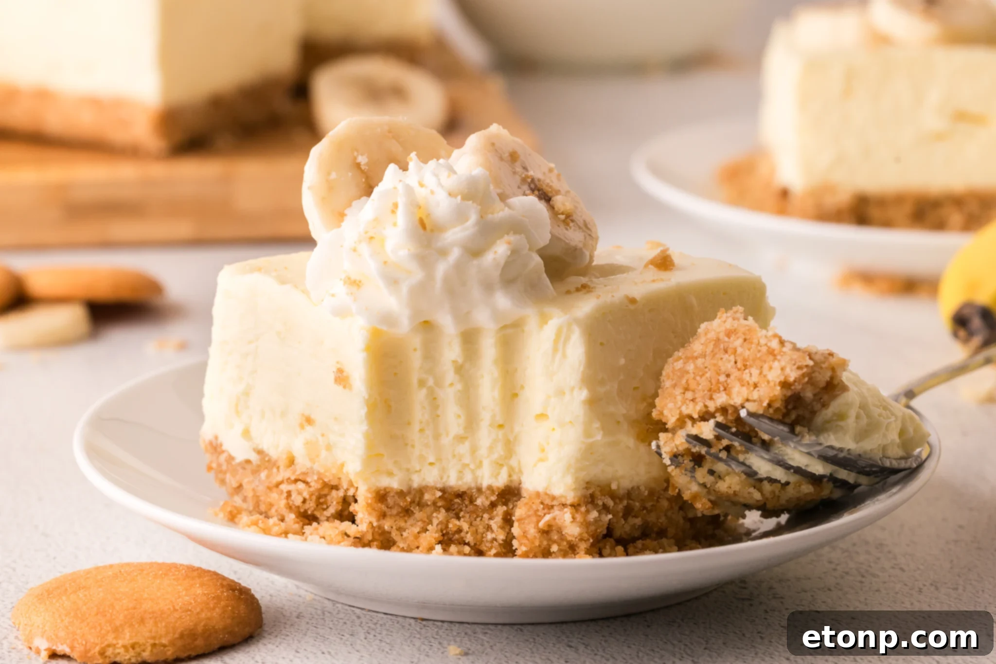 No Bake Banana Pudding Cheesecake Bar on a white plate with a fork bite taken out of it 