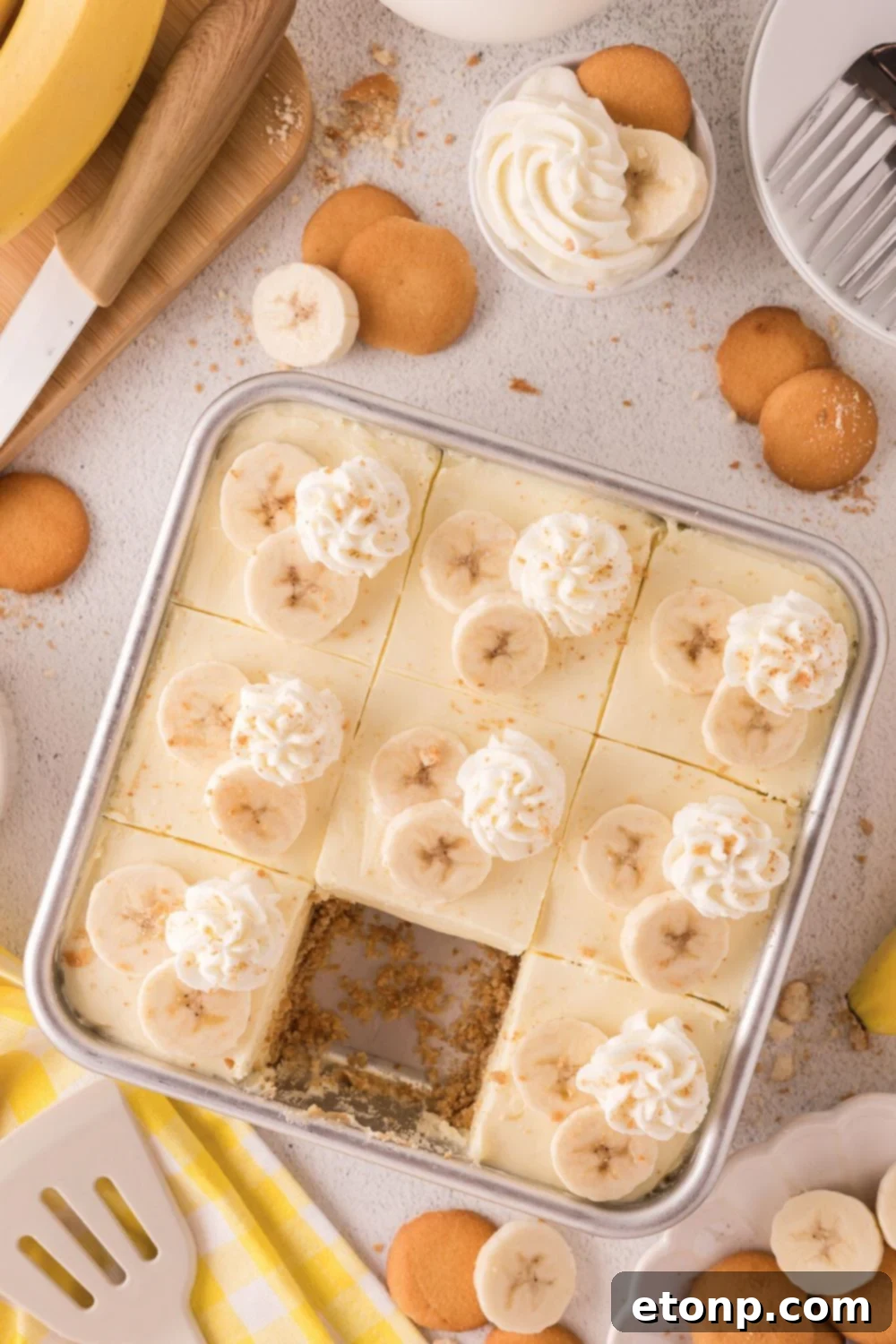 overhead look of table with No Bake Banana Pudding Cheesecake Bars in a pan with one taken out of the pan 