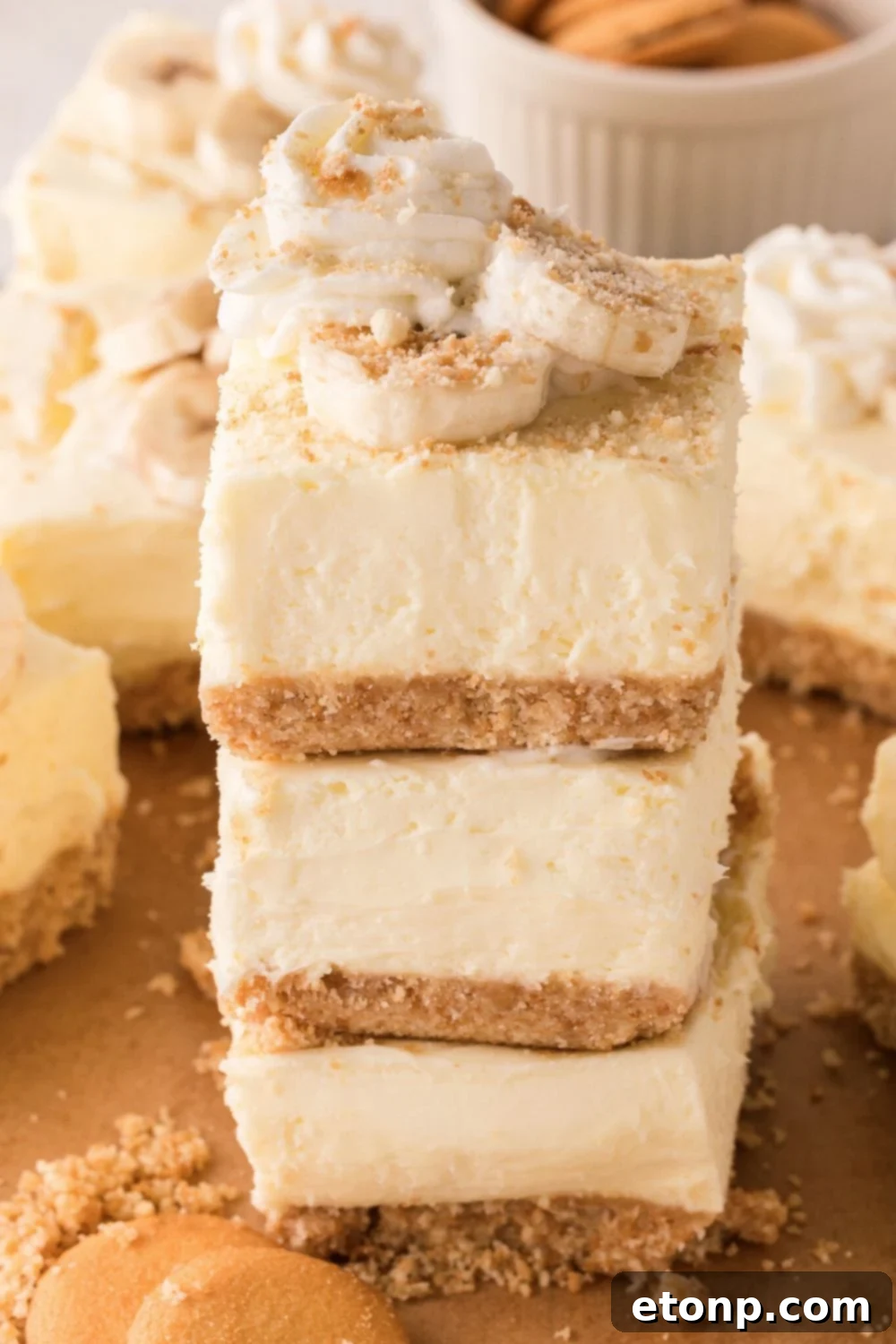No Bake Banana Pudding Cheesecake Bars stacked on a plate with more bars all around the table 