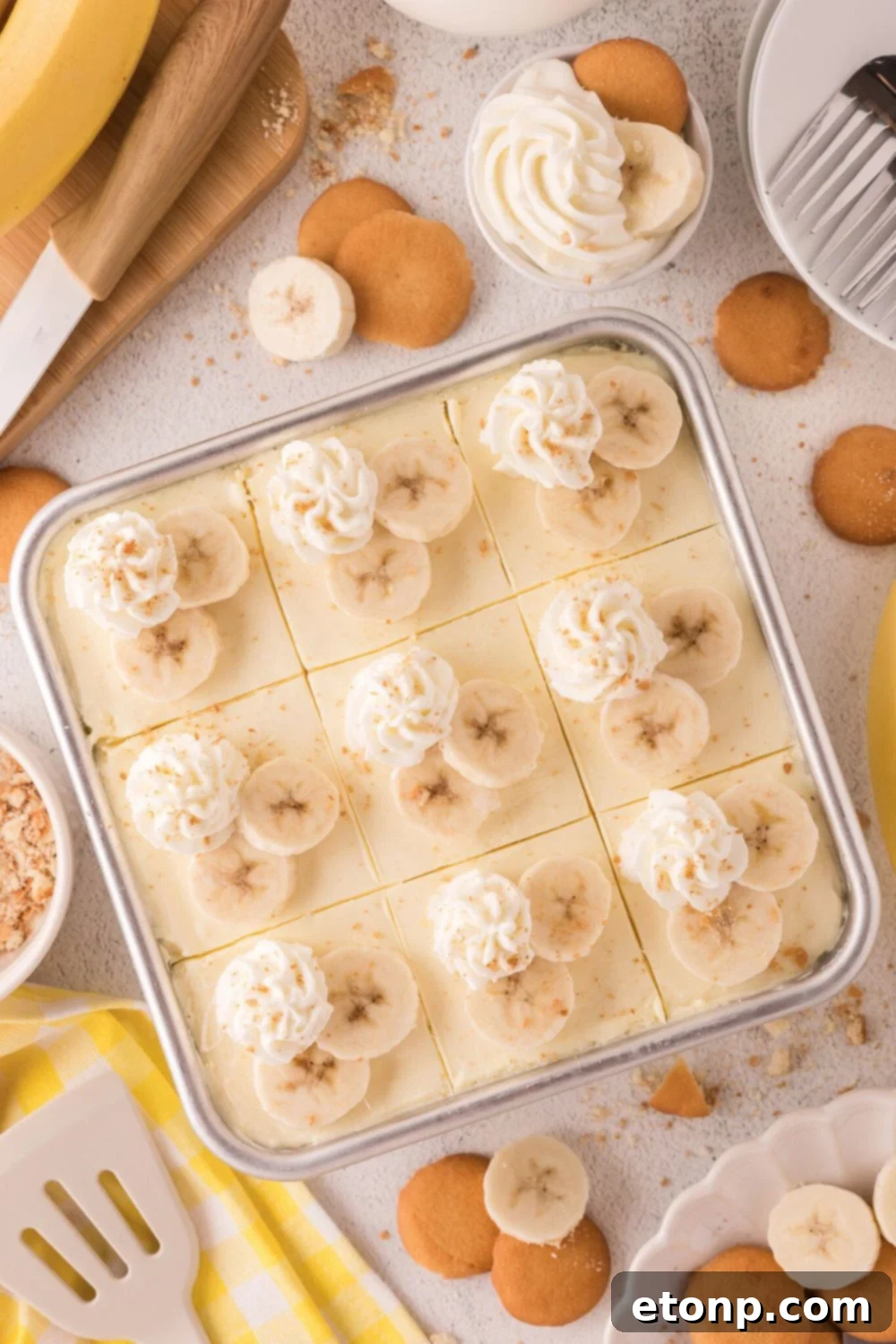 table with a pan of No Bake Banana Pudding Cheesecake Bars on it and vanilla wafers and bananas placed around the table 