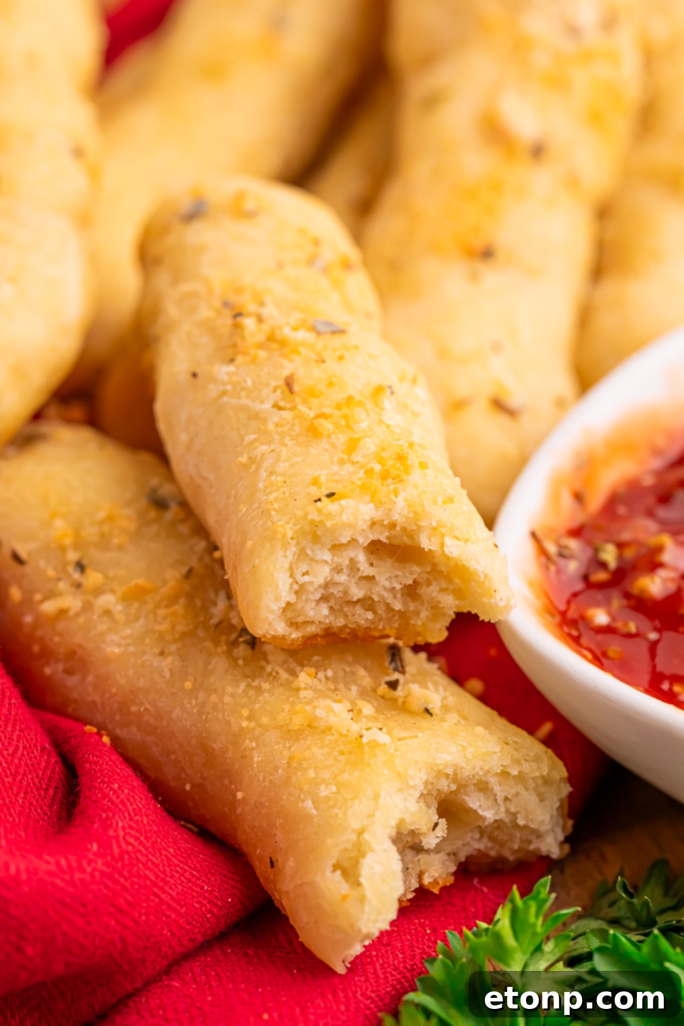 Easy Buttery Garlic Parmesan Breadsticks Two Ingredients 2 Freshly baked 2-Ingredient Garlic Parmesan Breadsticks on a table, one torn in half, with a small bowl of marinara sauce