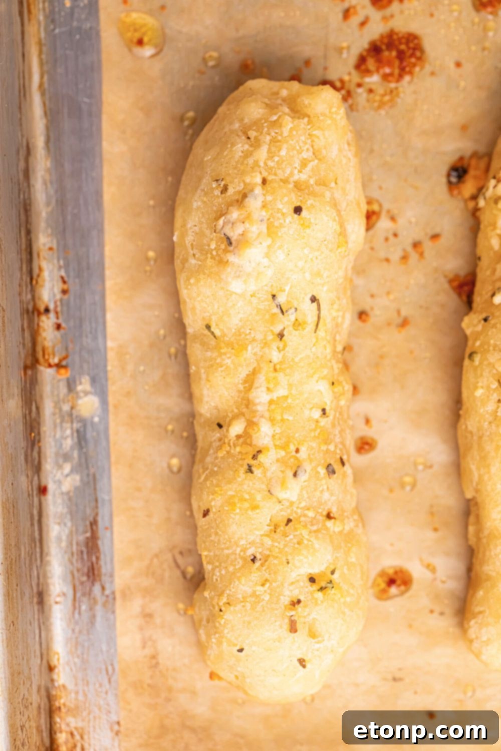 Easy Buttery Garlic Parmesan Breadsticks Two Ingredients 12 A single 2-Ingredient Garlic Parmesan Breadstick on a wooden table, showcasing its golden crust and soft interior.