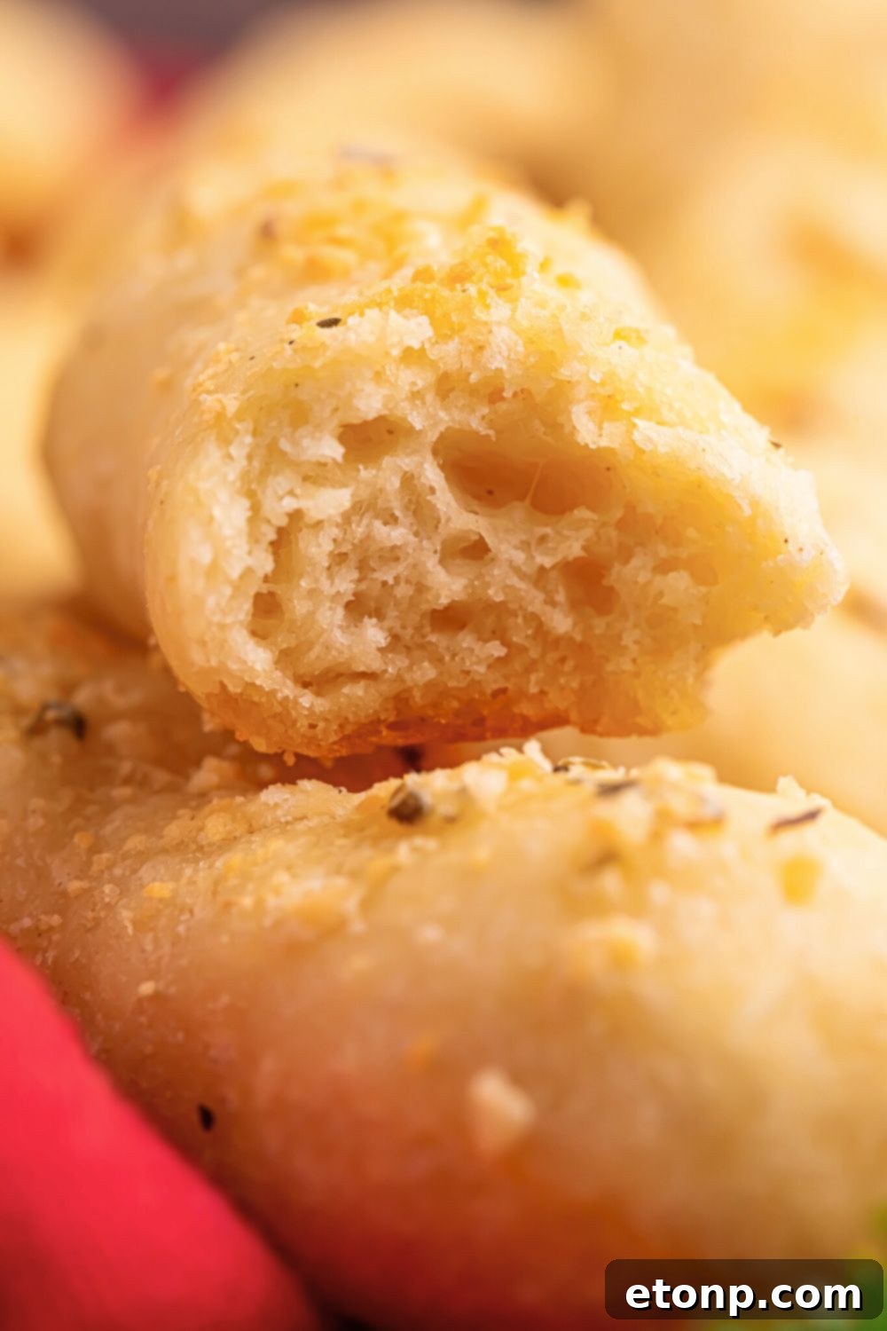 Easy Buttery Garlic Parmesan Breadsticks Two Ingredients 15 A 2-Ingredient Garlic Parmesan Breadstick with a bite taken out, resting next to a bowl of marinara sauce on a wooden table.