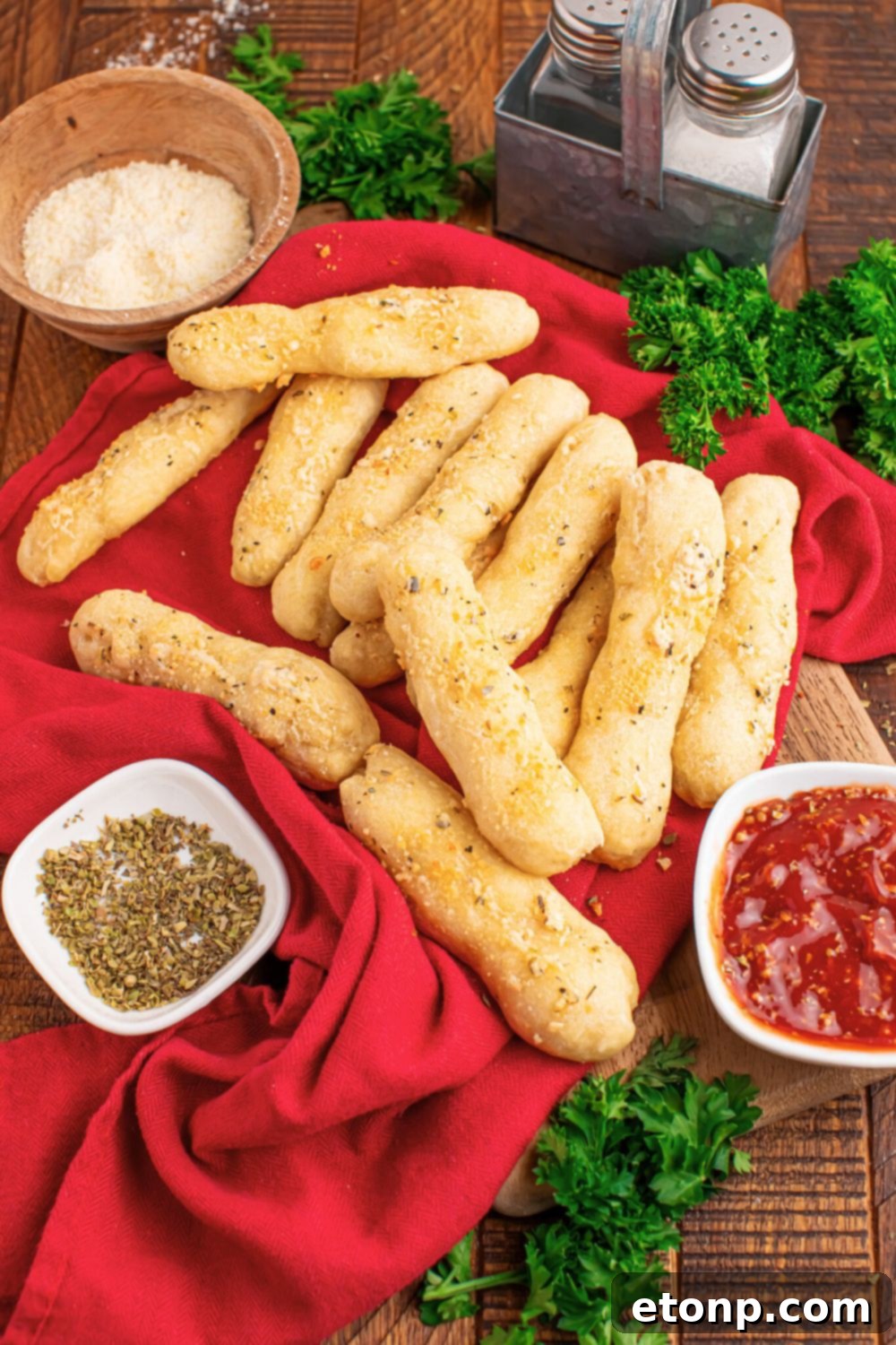Easy Buttery Garlic Parmesan Breadsticks Two Ingredients 18 A wooden table adorned with 2-Ingredient Garlic Parmesan Breadsticks, accompanied by small bowls of sauce, seasoning, and Parmesan cheese.