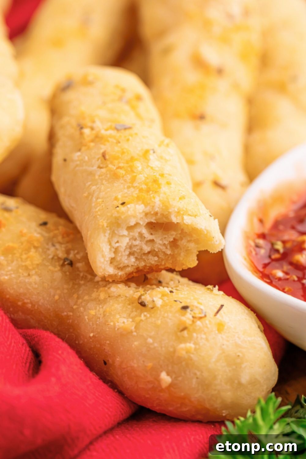 Easy Buttery Garlic Parmesan Breadsticks Two Ingredients 19 A 2-Ingredient Garlic Parmesan Breadstick with a bite taken out, accompanied by dipping sauce on the side.