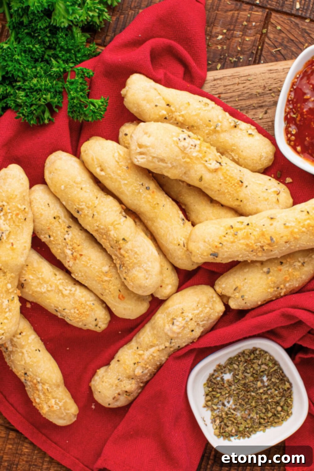 Easy Buttery Garlic Parmesan Breadsticks Two Ingredients 20 A 2-Ingredient Garlic Parmesan Breadstick on a wooden table, with a red towel underneath and fresh parsley as a garnish to the side.