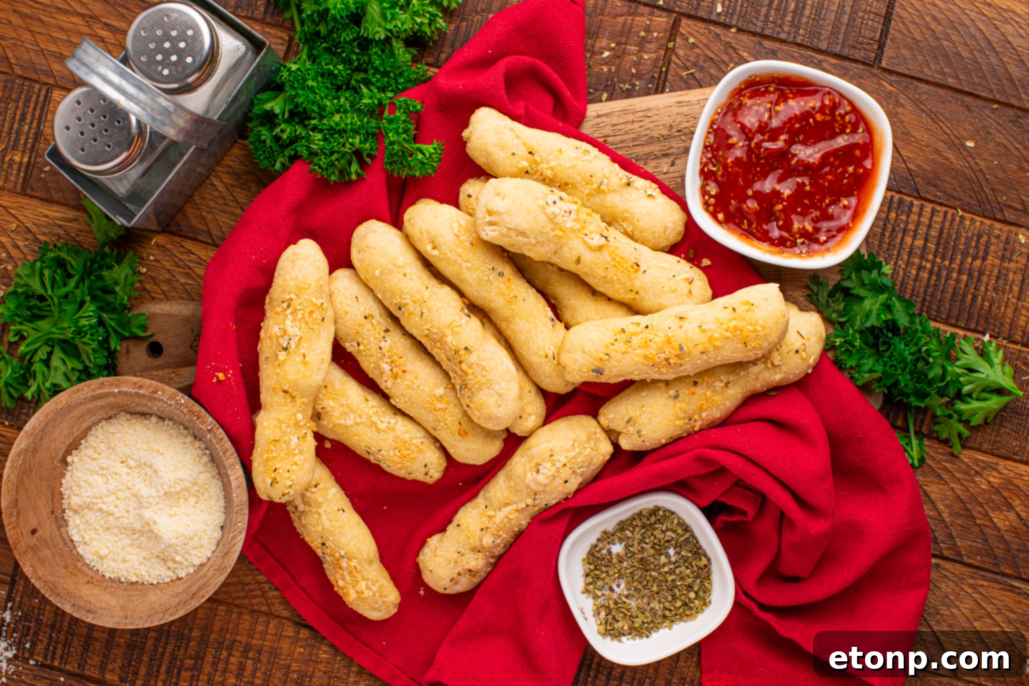 Easy Buttery Garlic Parmesan Breadsticks Two Ingredients 24 An overhead shot of breadsticks artfully arranged on a table, accompanied by small bowls of dipping sauce, Parmesan cheese, and oregano.