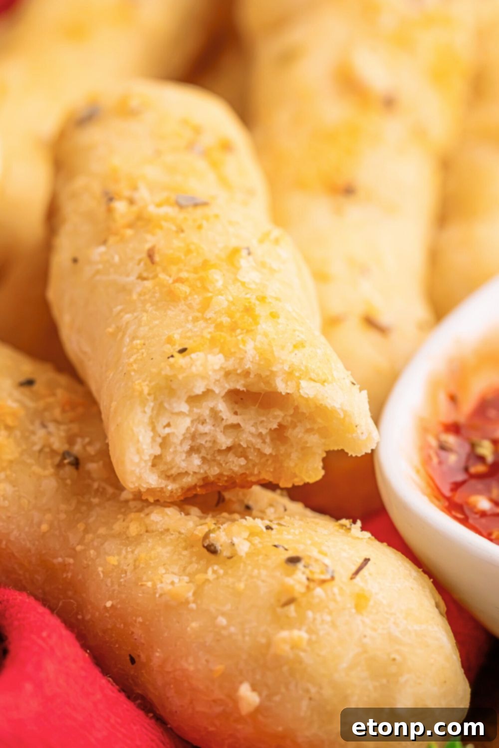 Easy Buttery Garlic Parmesan Breadsticks Two Ingredients 4 A 2-Ingredient Garlic Parmesan Breadstick with a bite taken out, resting next to a bowl of marinara sauce on a table