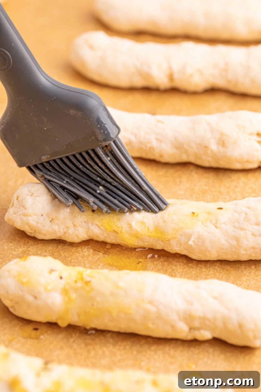 Easy Buttery Garlic Parmesan Breadsticks Two Ingredients 10 A hand brushing raw 2-Ingredient Garlic Parmesan Breadsticks with melted butter on a baking tray