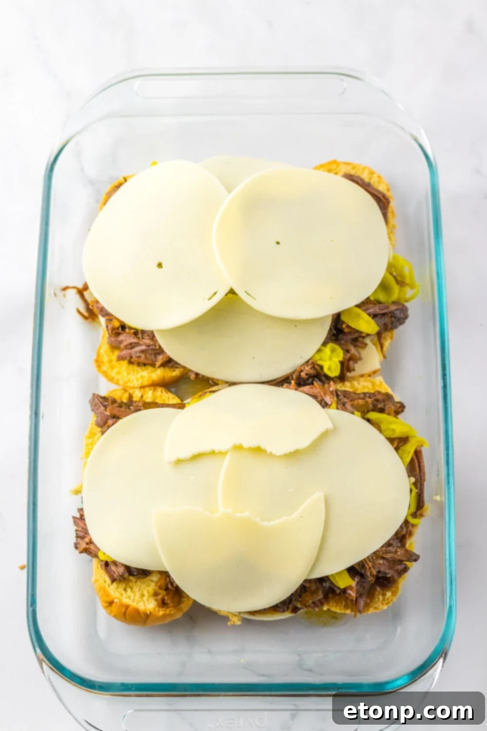 provolone cheese on top of meat and peppers in a casserole pan