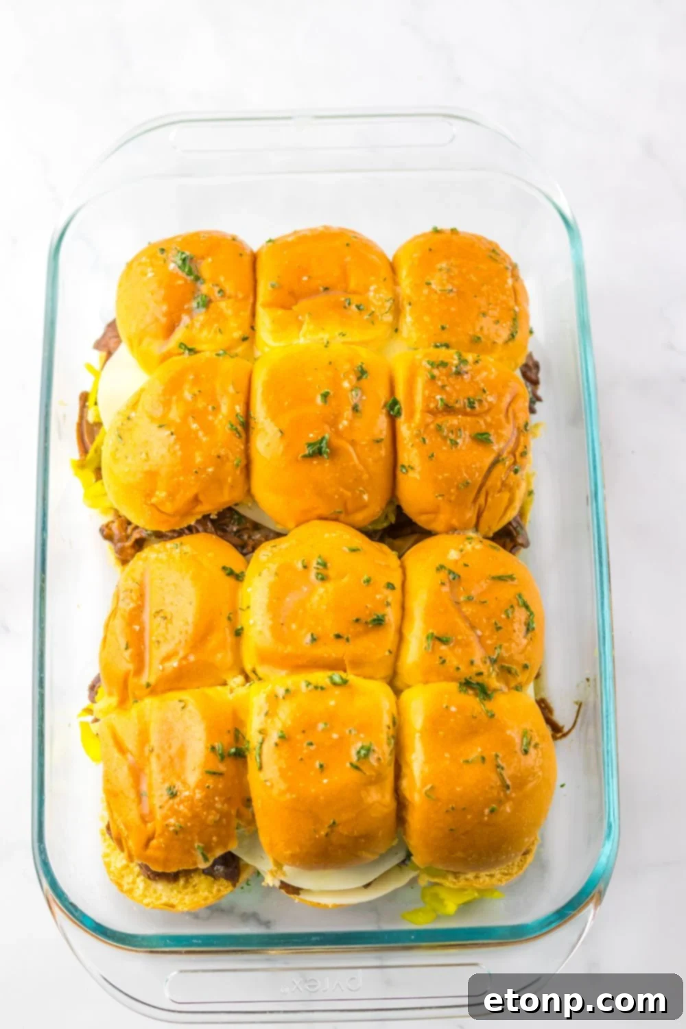 Slow Cooker Mississippi Pot Roast Sliders assembled and being topped with parsley butter