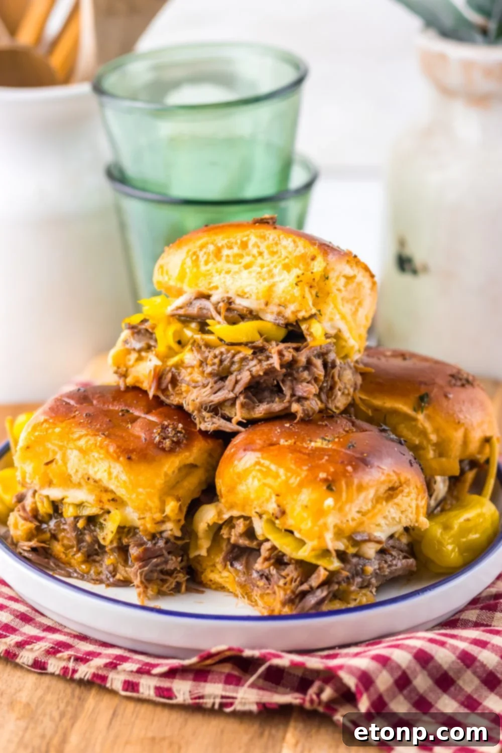  Mississippi Pot Roast Sliders stacked on a plate with glasses behind the plate 