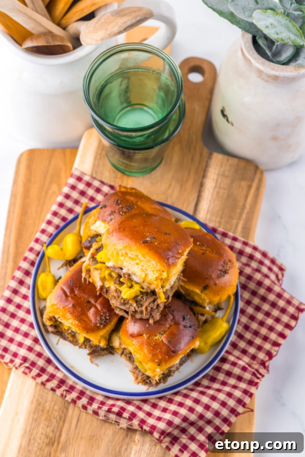 Slow Cooker Mississippi Pot Roast Sliders on a plate with some dishes behind the plate full of burgers 