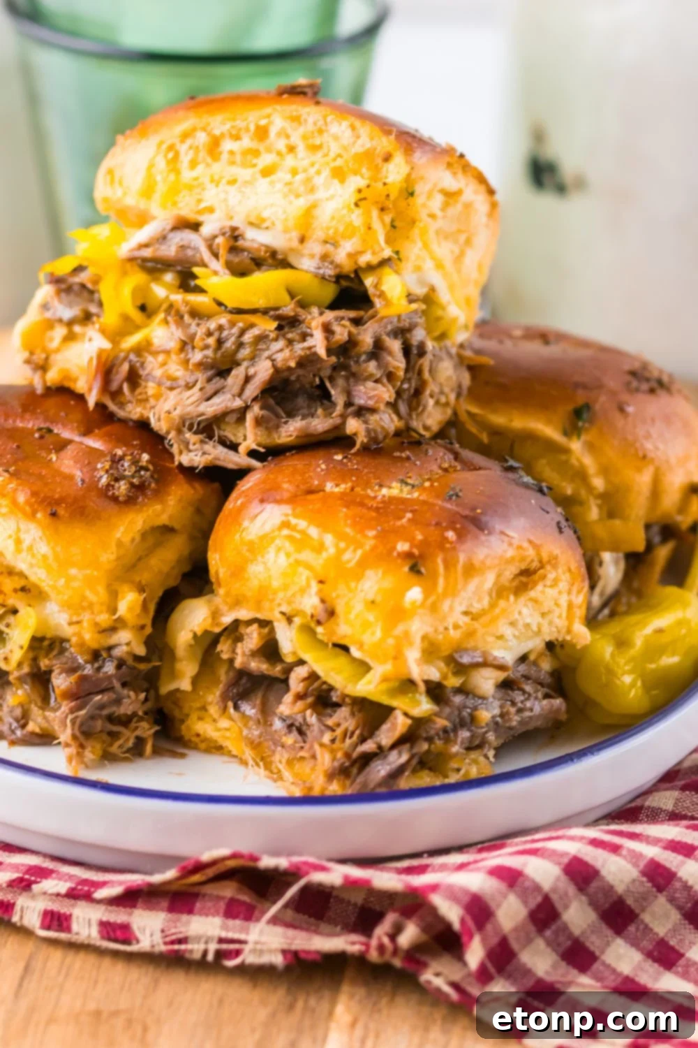 Slow Cooker Mississippi Pot Roast Sliders stacked on plate with a red checkered towel under the plate 
