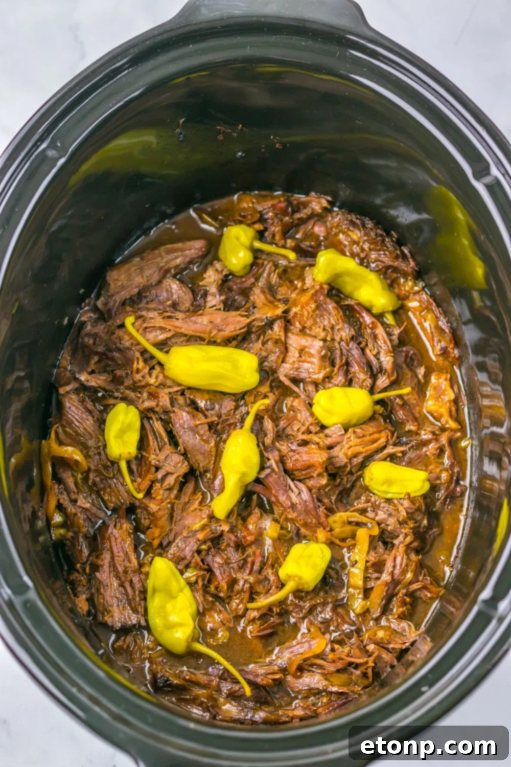 Slow Cooker Mississippi Pot Roast in a slow cooker with more peppers on top 