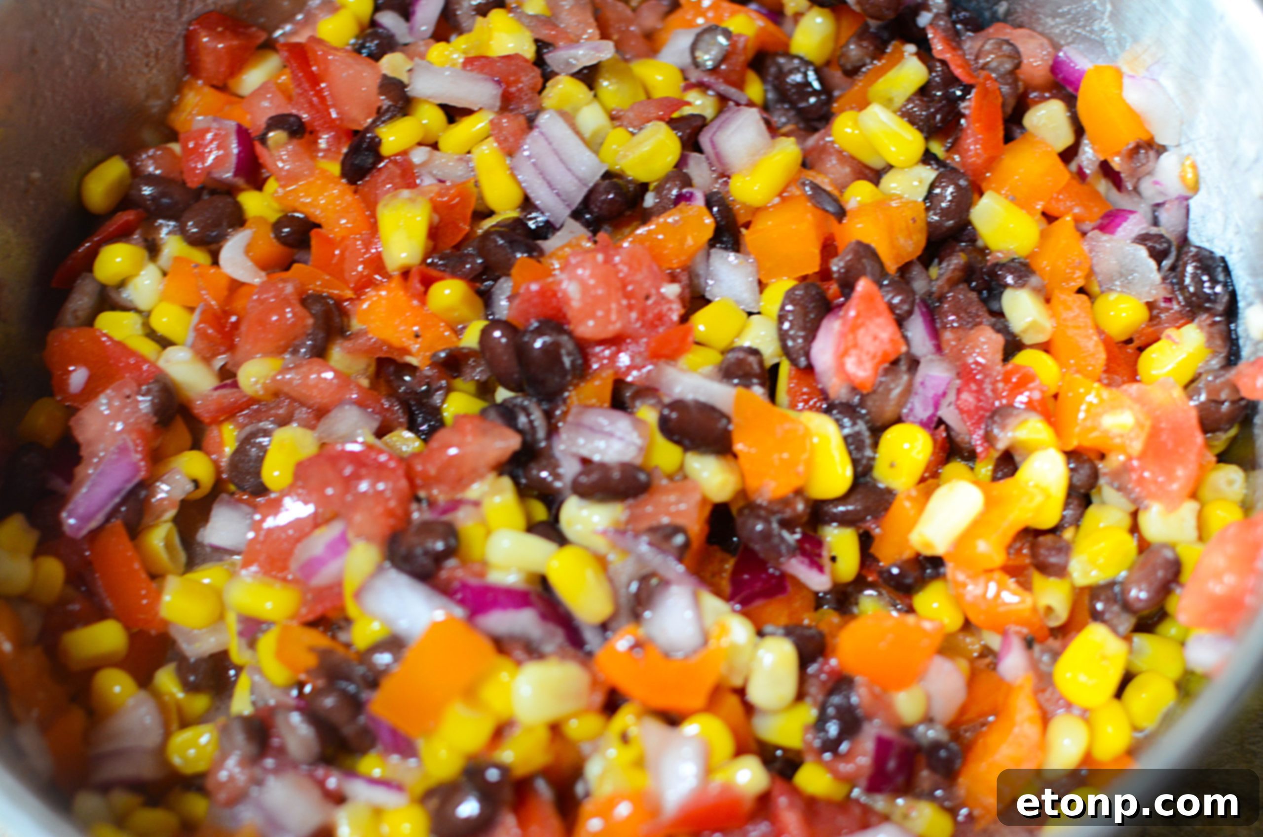 All the fresh ingredients for Cowboy Caviar laid out on a cutting board, including beans, corn, bell pepper, tomatoes, and cilantro.