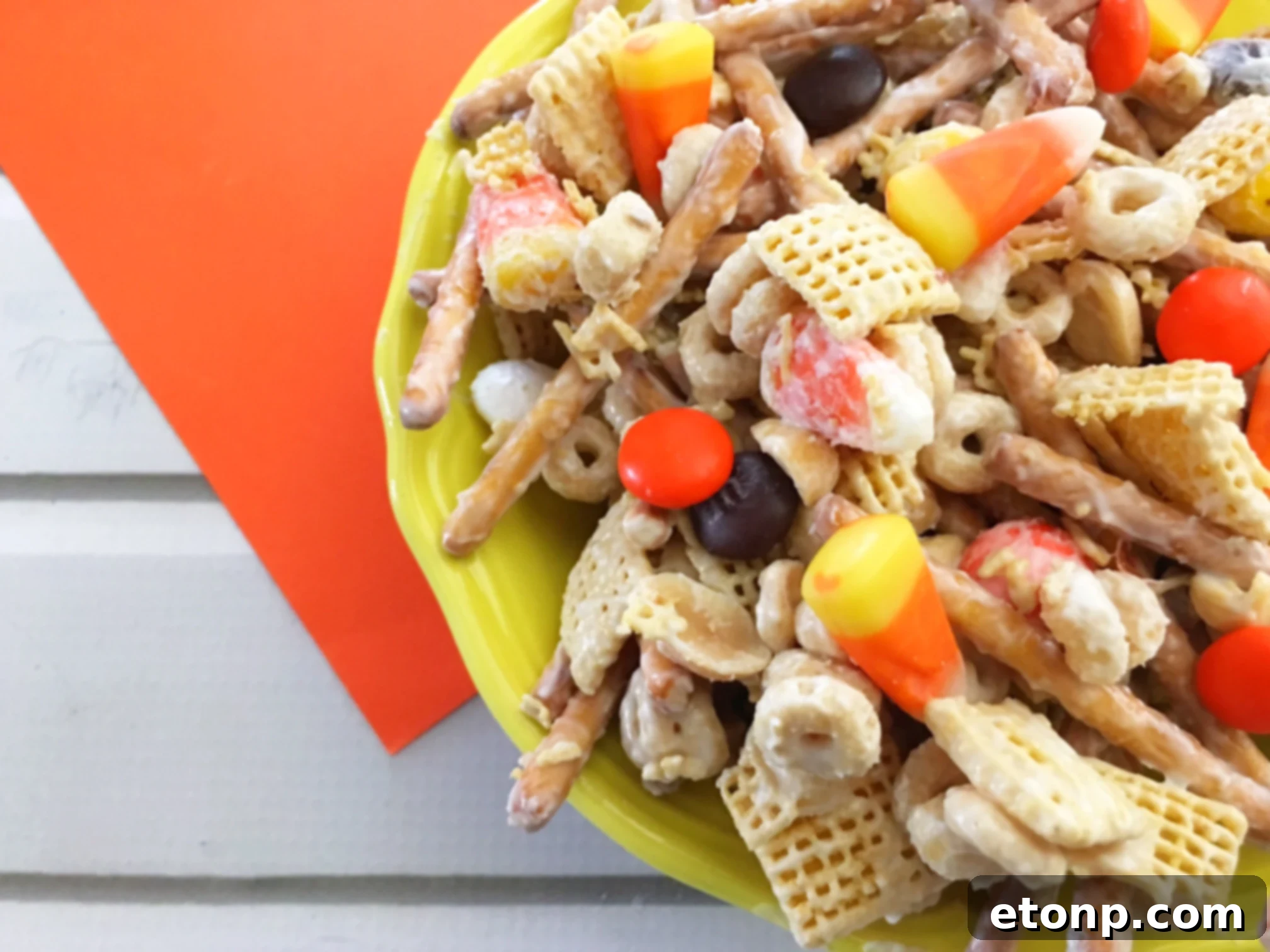 A vibrant assortment of sweet and salty Fall Harvest Crack ingredients spread on a tray, featuring pretzels, colorful M&Ms, candy corn, and cereals.