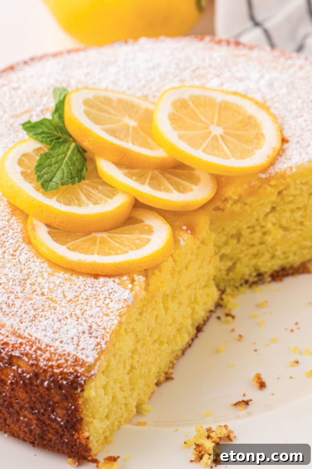 Effortless Italian Lemon Ricotta Cake: Light and Lemony Perfection 18 A full Italian Lemon Ricotta Cake sits on a table, with a few slices already taken and decorative lemon wedges placed on top, ready for enjoyment.