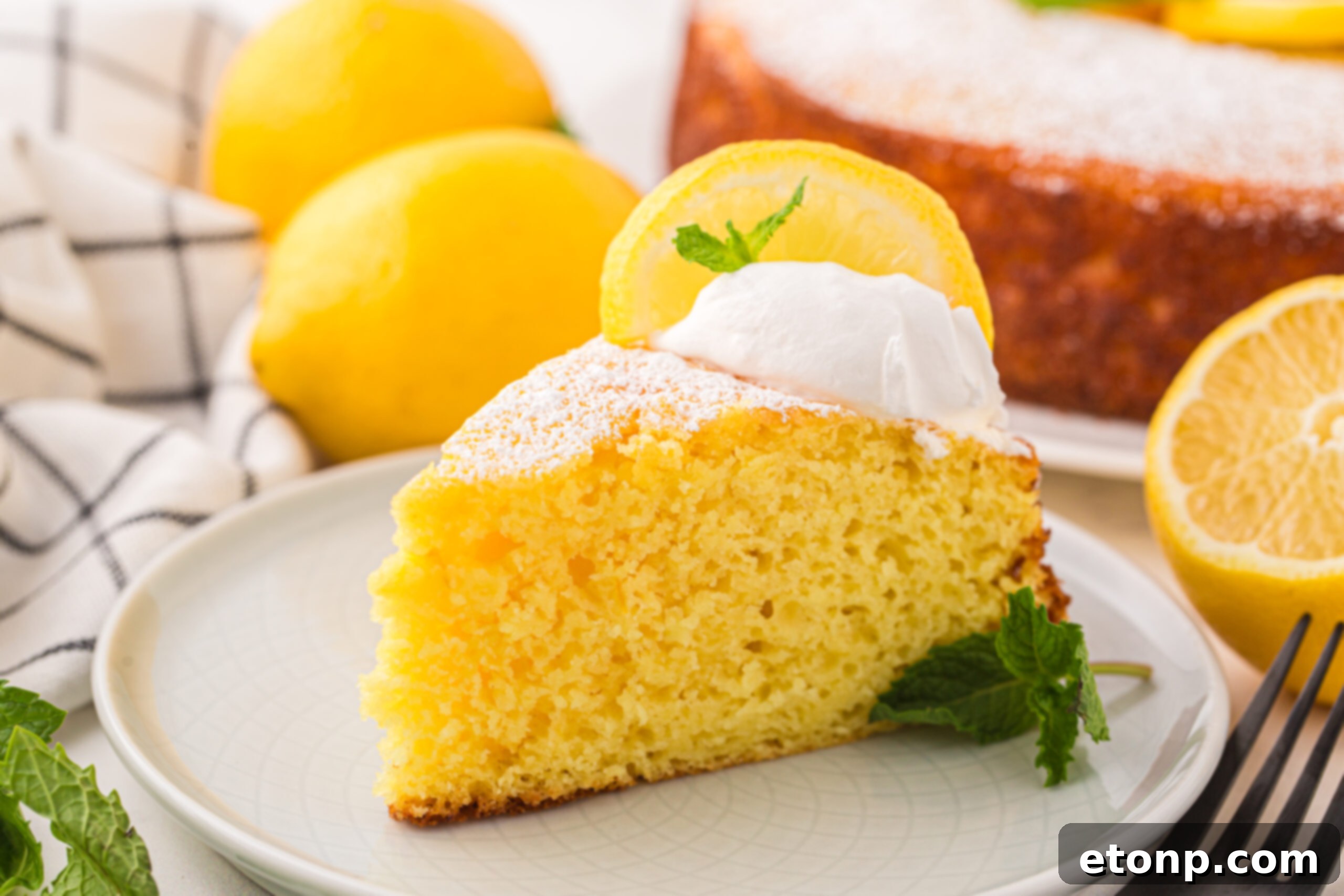 Effortless Italian Lemon Ricotta Cake: Light and Lemony Perfection 22 A beautiful slice of Italian Lemon Ricotta Cake on a plate, with whole lemons displayed behind it on a table, and the remainder of the cake in the background, creating an inviting scene.