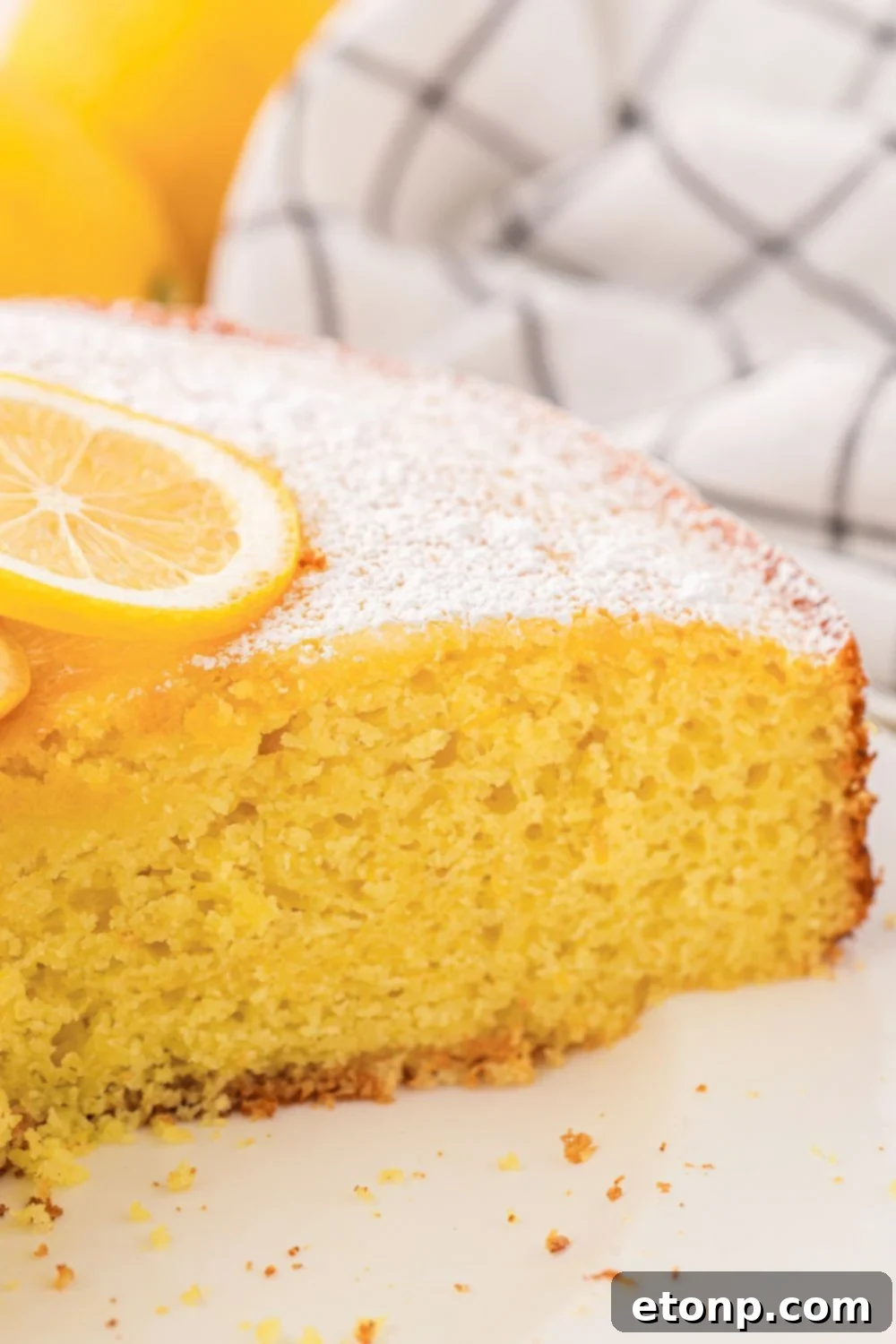 Effortless Italian Lemon Ricotta Cake: Light and Lemony Perfection 6 A beautifully presented slice of Italian Lemon Ricotta Cake adorned with a thin lemon slice, resting on a white plate on a wooden table.