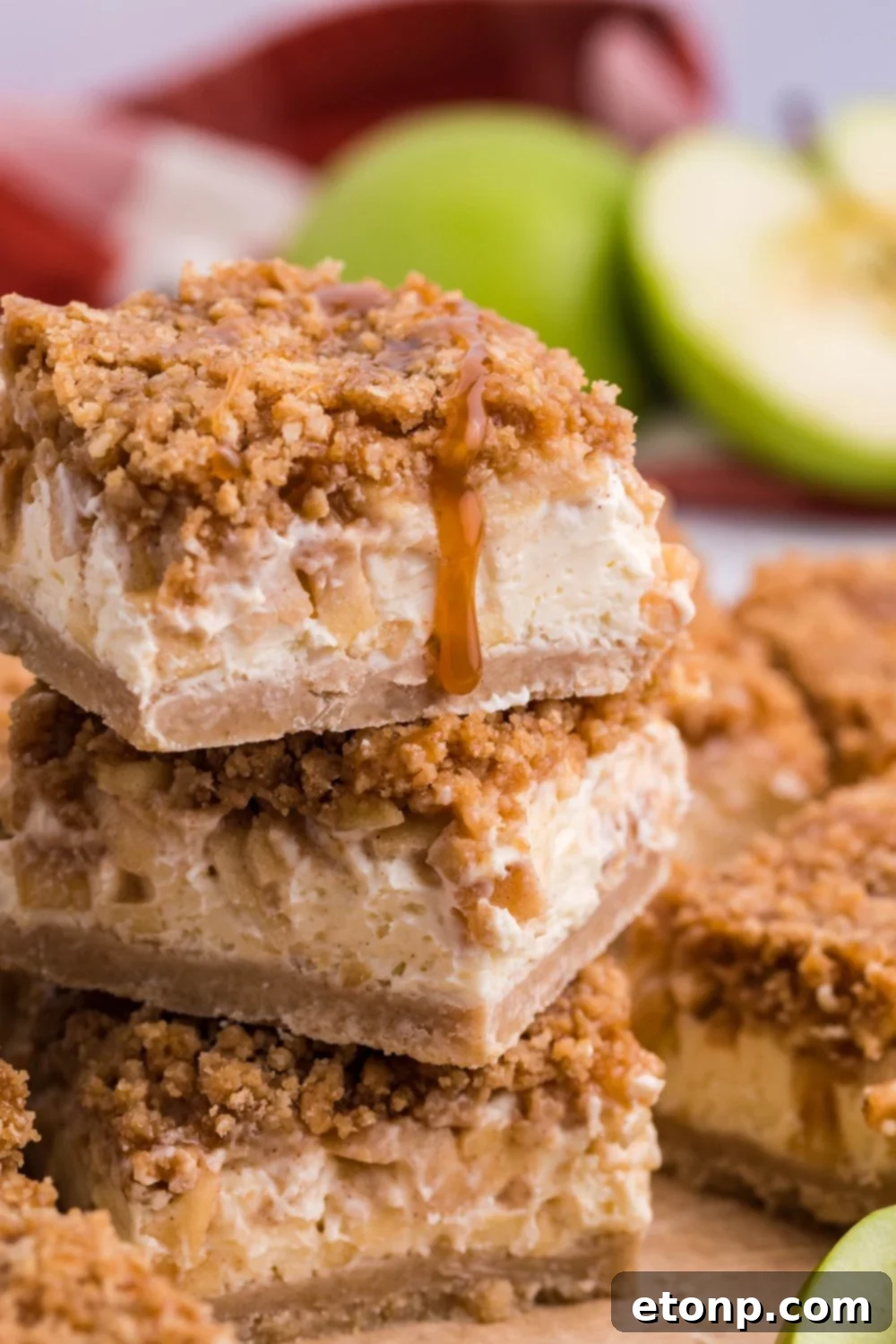 Caramel Apple Cheesecake Bars stacked on top of one another on table with apple sliced in half to side