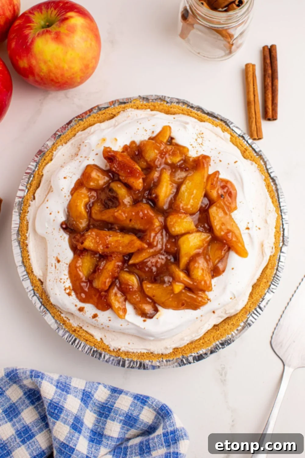 overhead look of table with No Bake Apple Cheesecake pie and apples and cinnamon sticks to side 