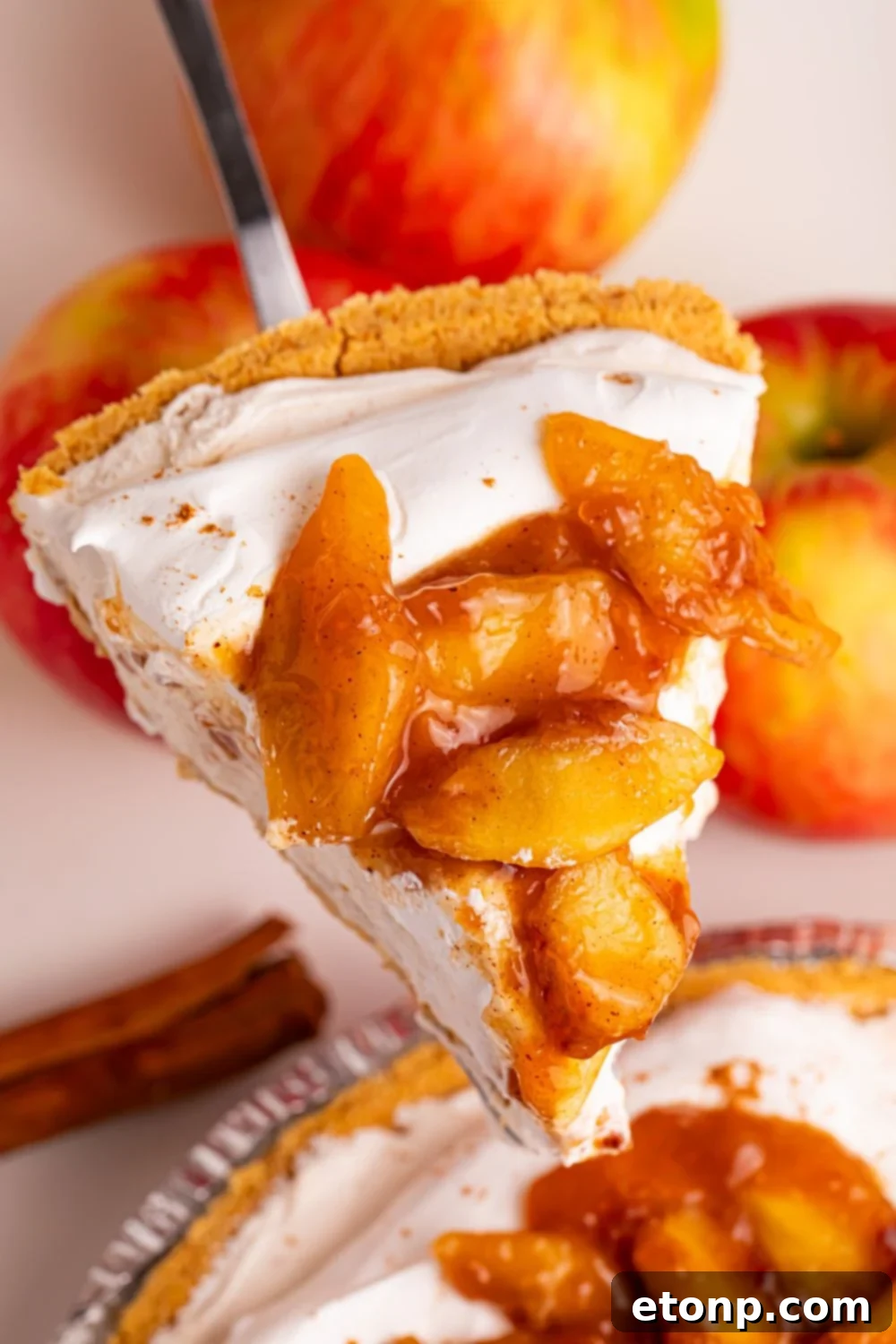 slice of No Bake Apple Cheesecake pie slice being lifted above pie dish on a table 
