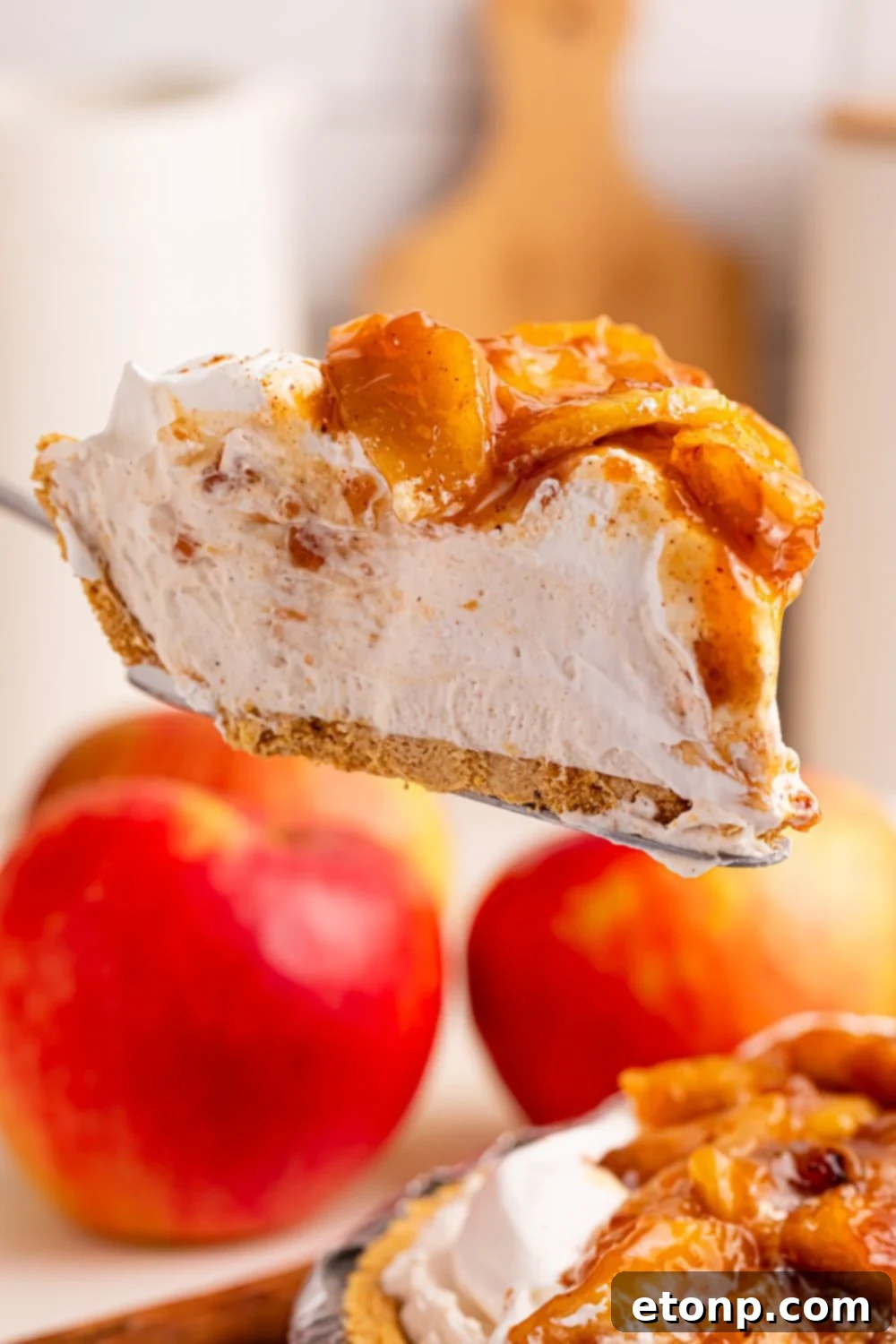 slice of No Bake Apple Cheesecake pie on spatula with red apples 