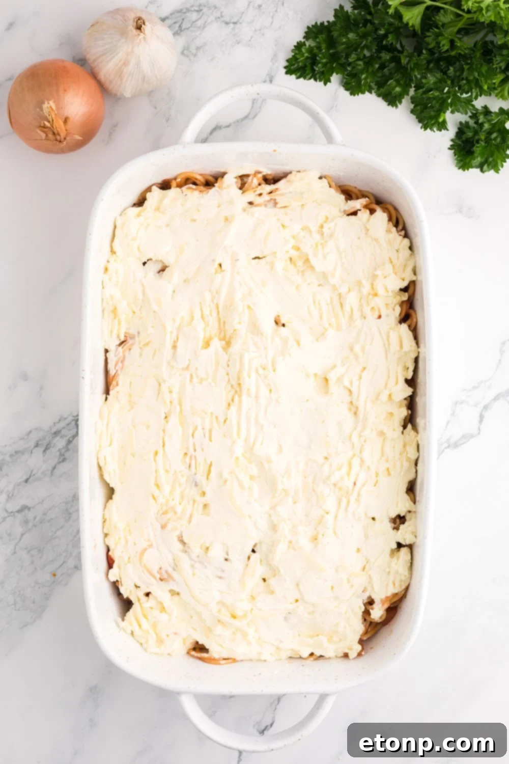Million Dollar Spaghetti Casserole being assembled in a pan on table 