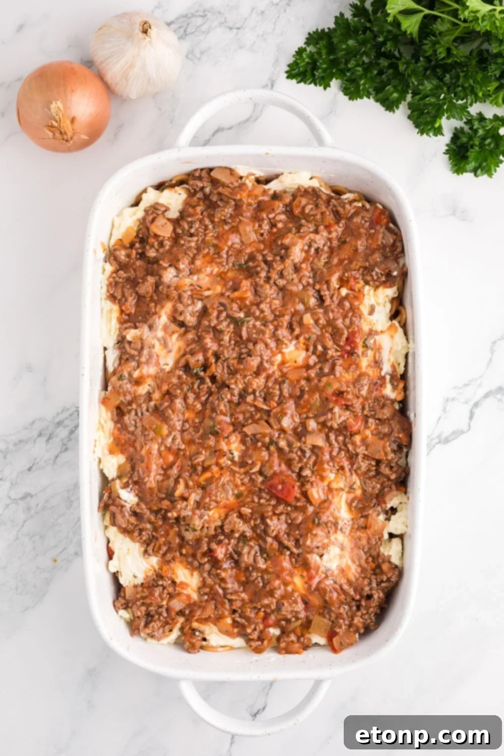 Million Dollar Spaghetti Casserole being assembled in a pan on table 