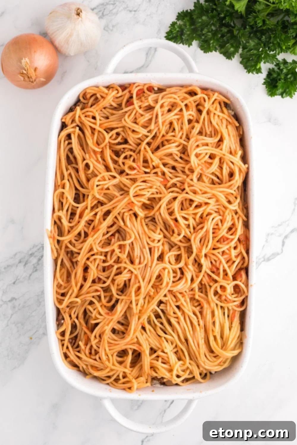 Million Dollar Spaghetti Casserole being assembled in a pan on table 