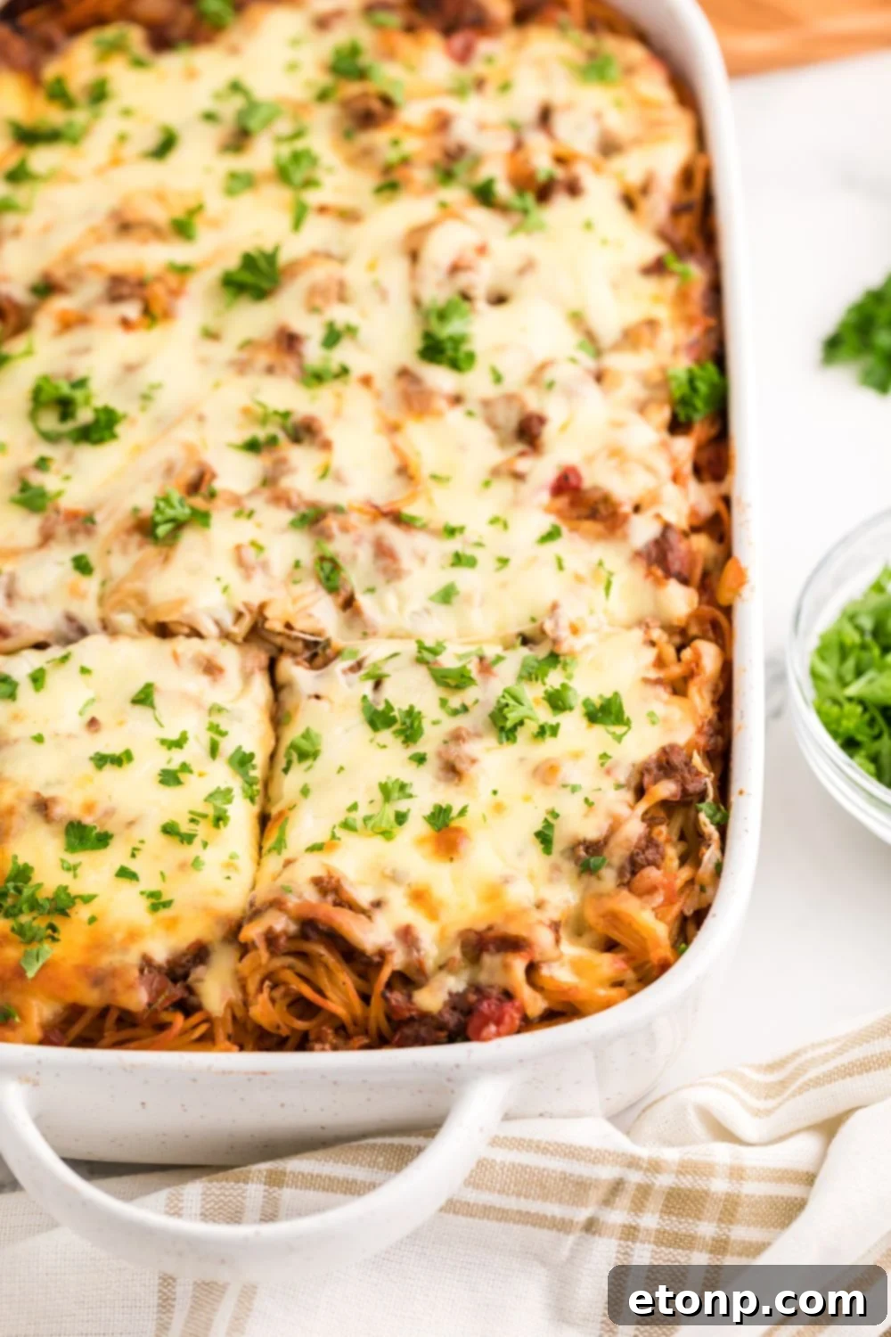 Million Dollar Spaghetti Casserole in pan with parsley sprinkled on top cut into squares 