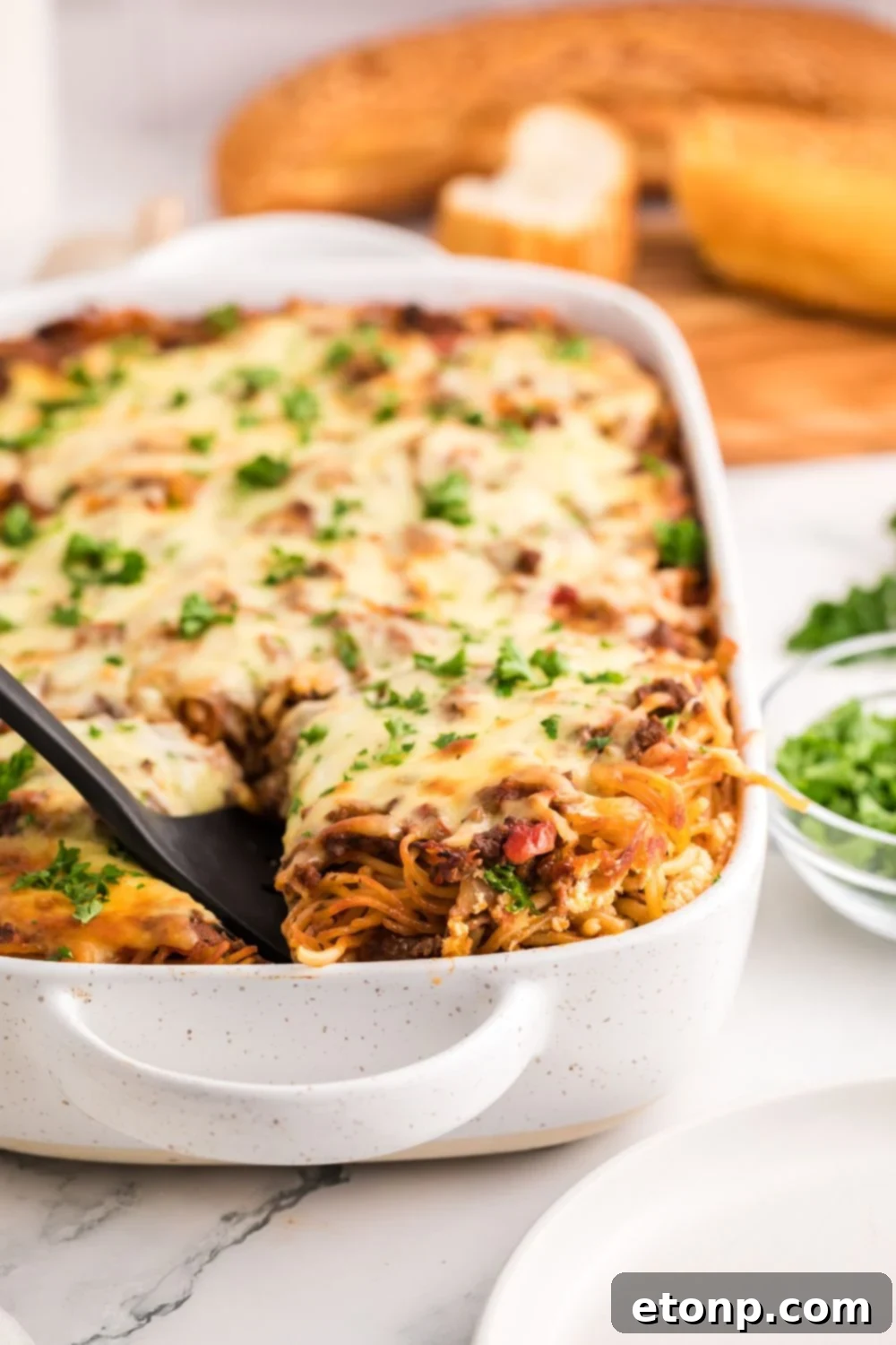 Million Dollar Spaghetti Casserole in a pan with bread behind on a cutting board 