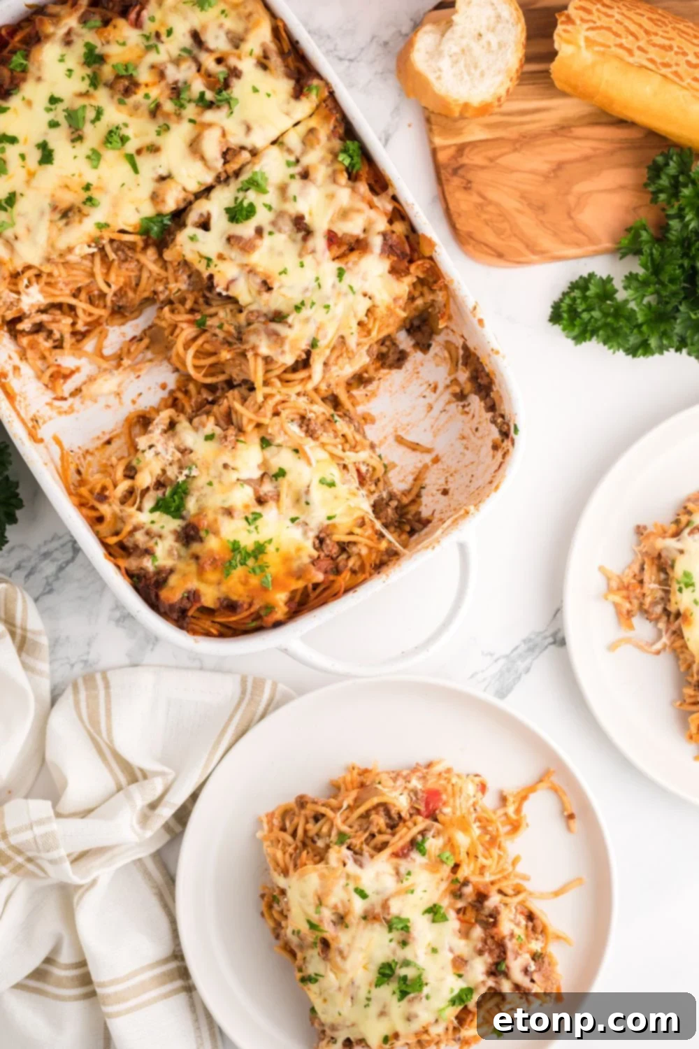 Million Dollar Spaghetti Casserole in pan with more spaghetti on plates with parsley to side and sliced bread 