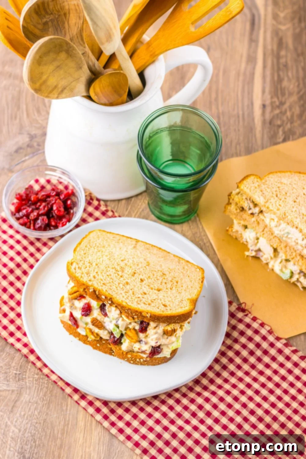 Thanksgiving Turkey Salad on plates with another sandwich on a cutting board, and a bowl of cranberries to side 