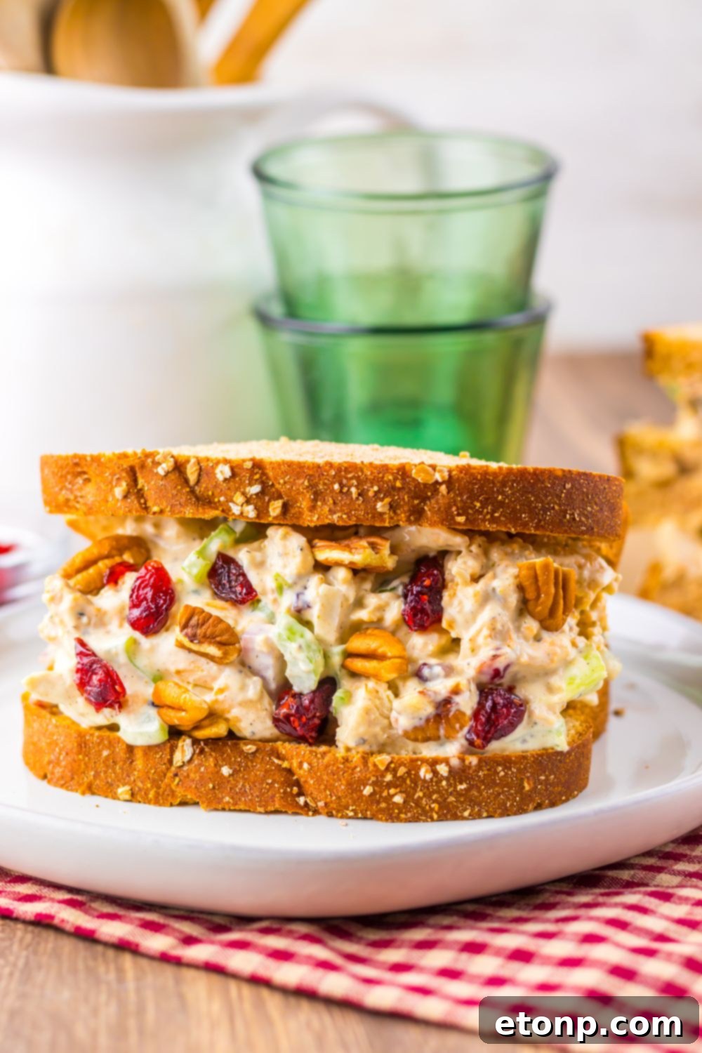 front view of wooden table with a plate with a thick Thanksgiving Turkey Salad sandwich on plate, and two glasses stacked together sitting behind it on the table 