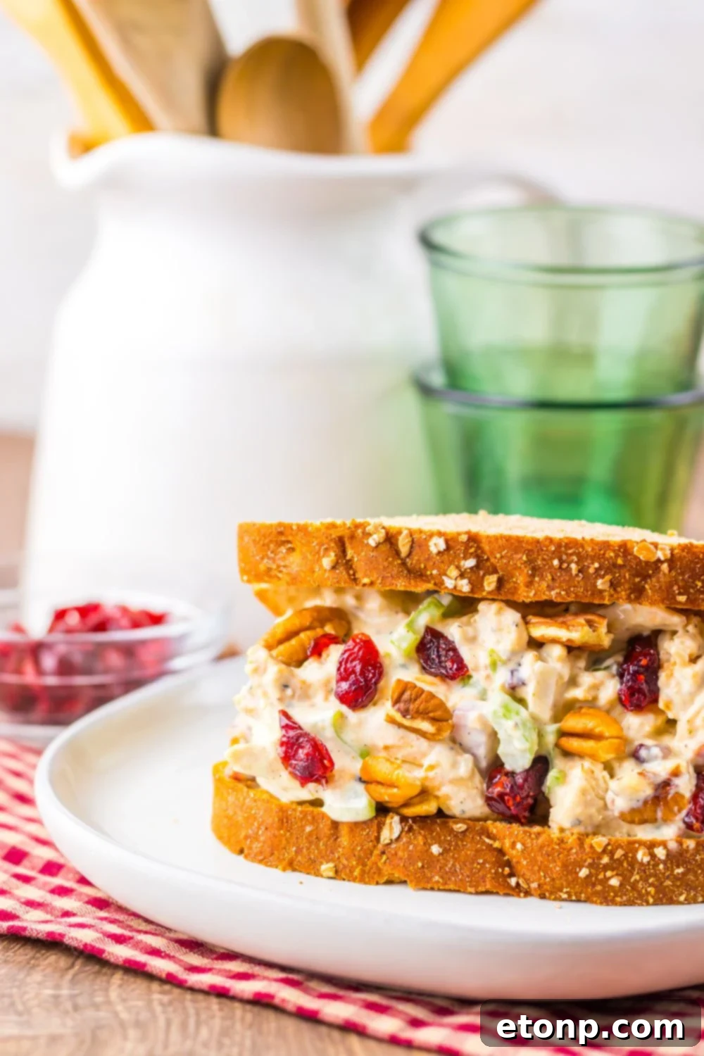 Turkey salad sandwich with cranberries, pecans, and celery on whole grain bread, served on a white plate with a rustic kitchen background