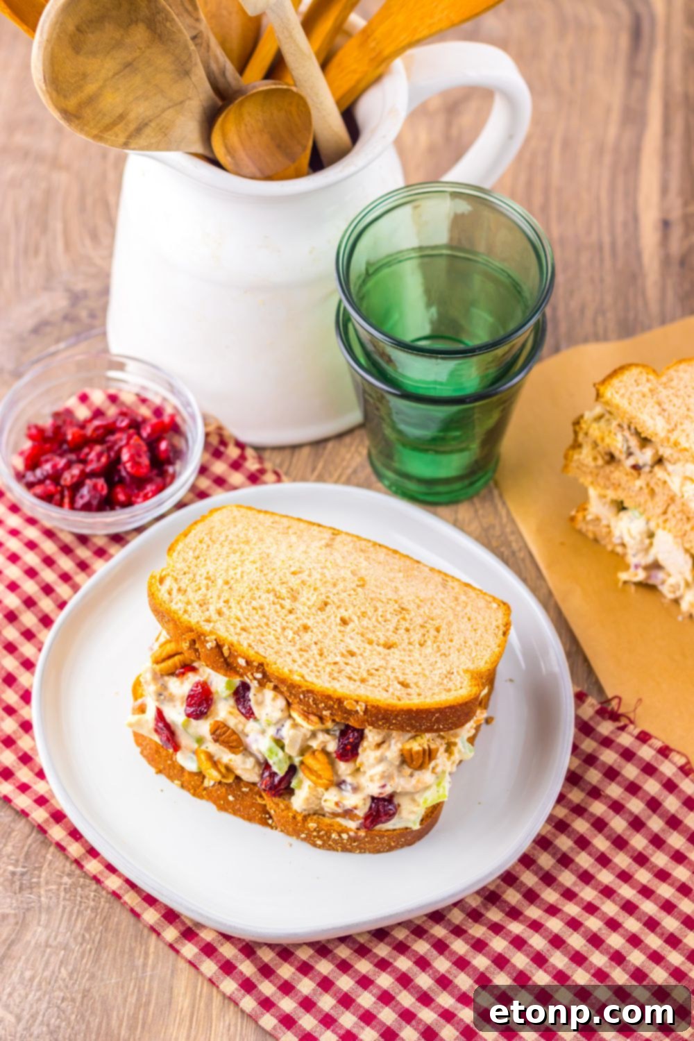 Thanksgiving Turkey Salad sandwiches on plates, with cranberries in a bowl to side and container full of kitchen utensils in background 
