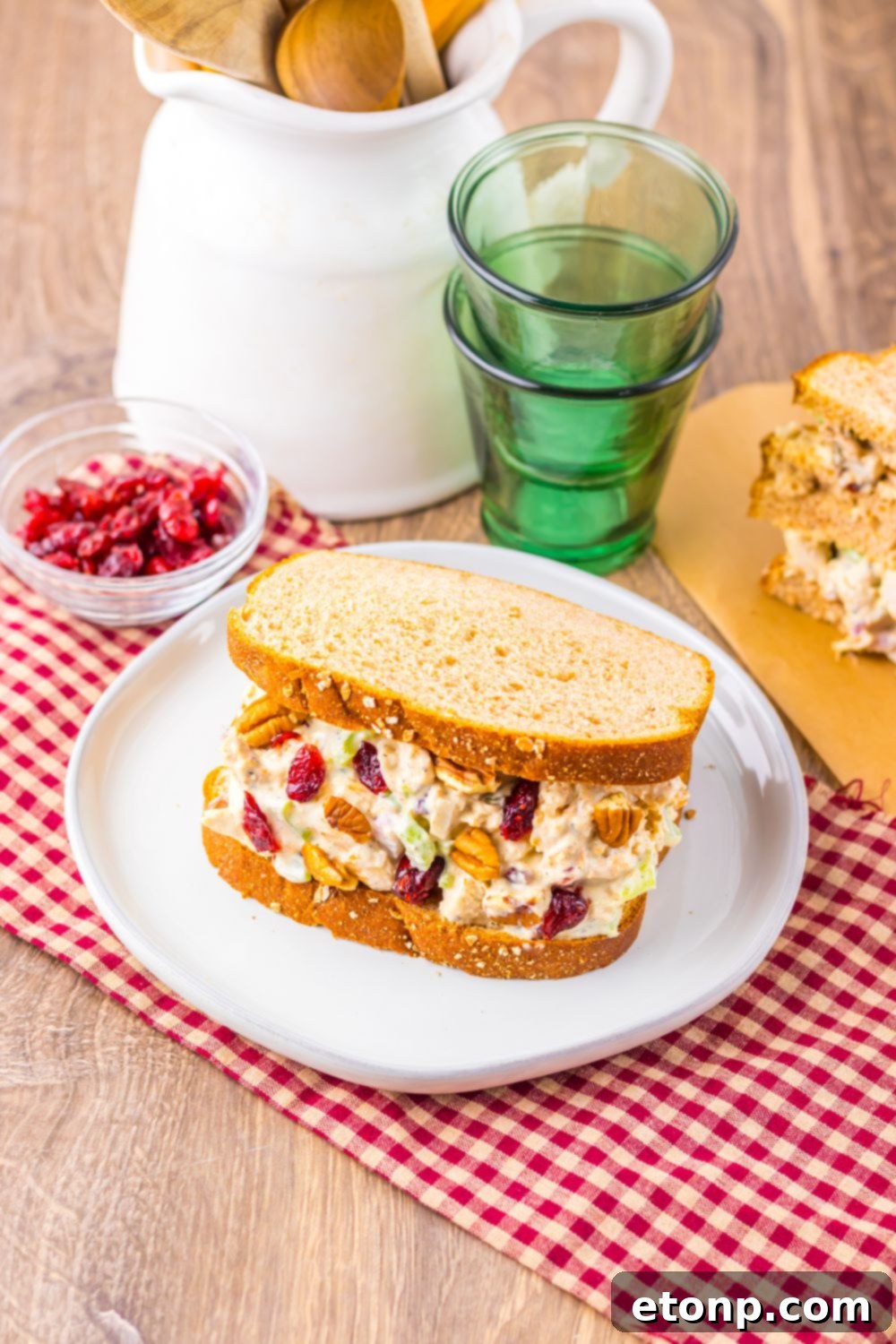 Thanksgiving Turkey Salad sandwiches pn plates with glasses, and a bowl of cranberries to side by a napkin