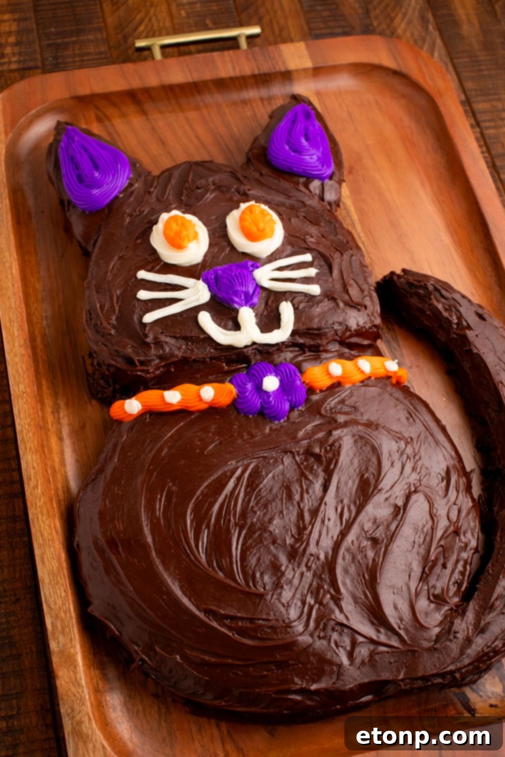 A homemade Halloween cake skillfully crafted into the shape of a black cat, resting on a rustic cutting board.