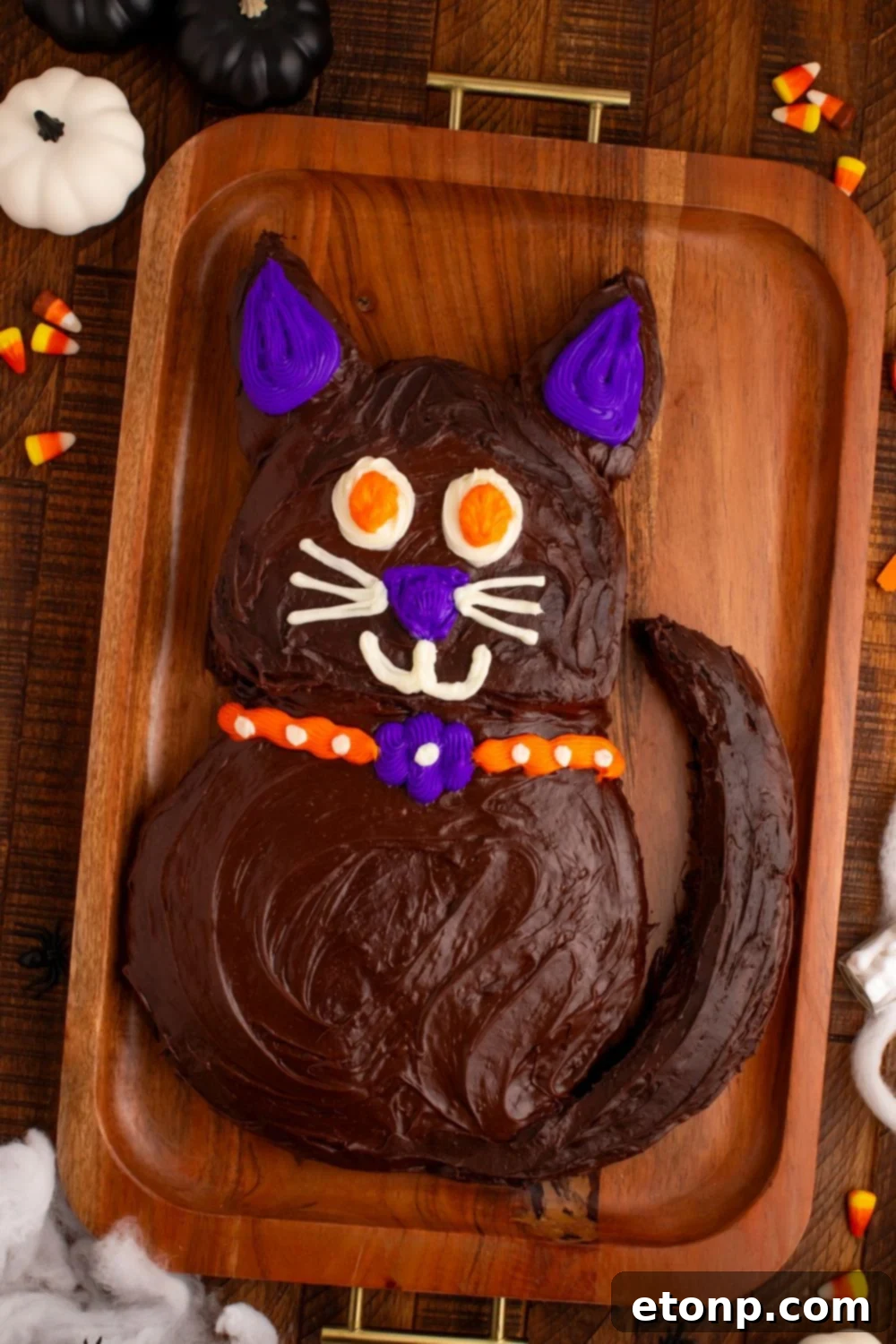 The Easy Halloween Black Cat Cut Out Cake presented on a tray, surrounded by decorative fake pumpkins and candy corn, creating a festive autumn scene.