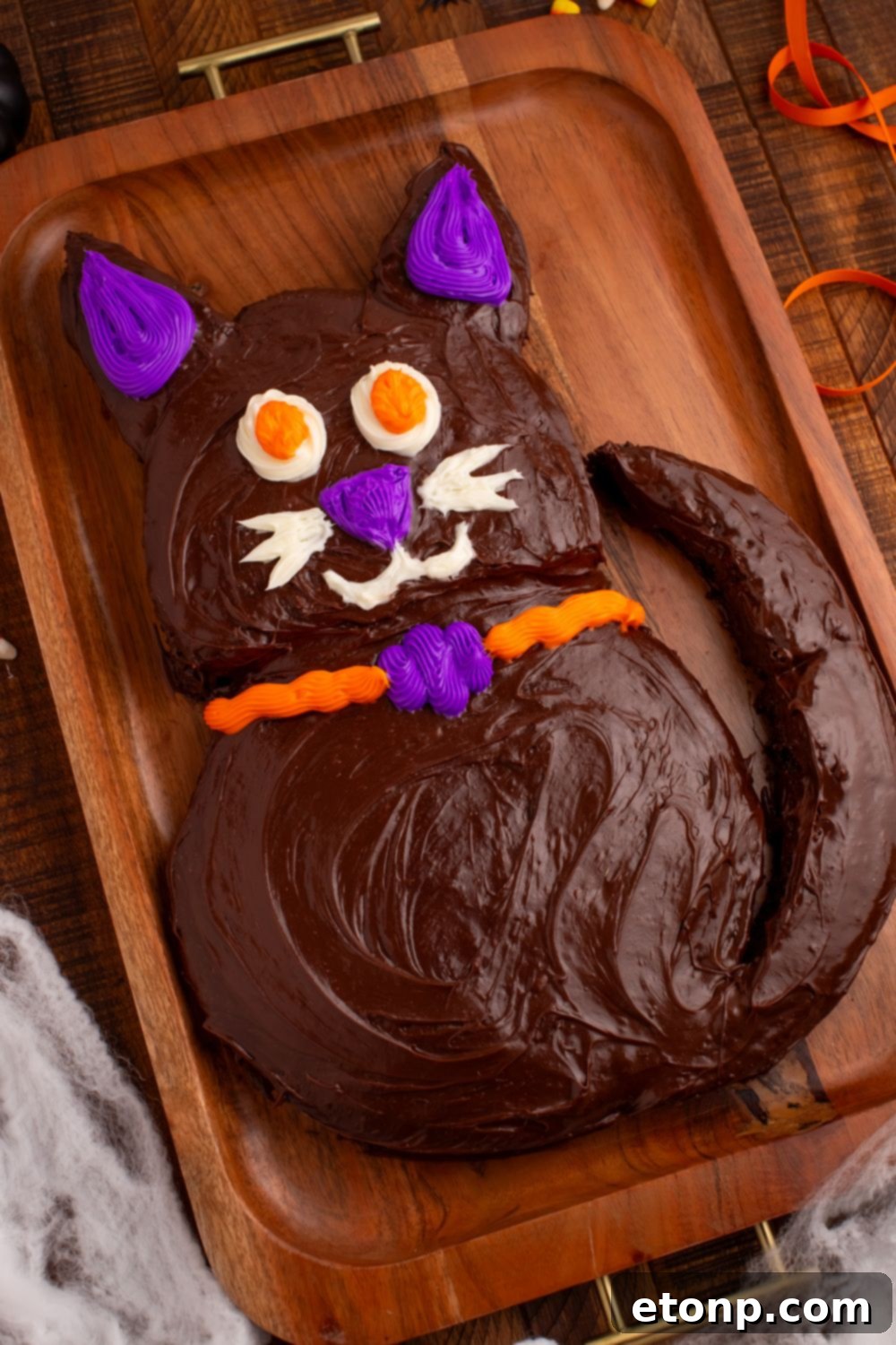 The Easy Halloween Black Cat Cut Out Cake on a serving tray, adorned with delicate fake spider webs draped around its base, enhancing the spooky ambiance.