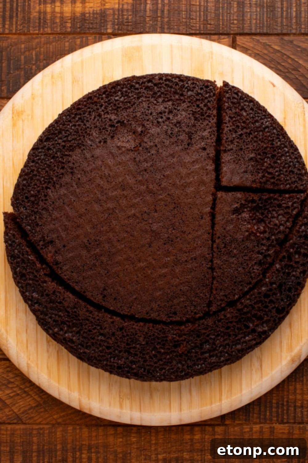 A round cake being carefully cut into distinct pieces to form the various components of a cat's body and features.