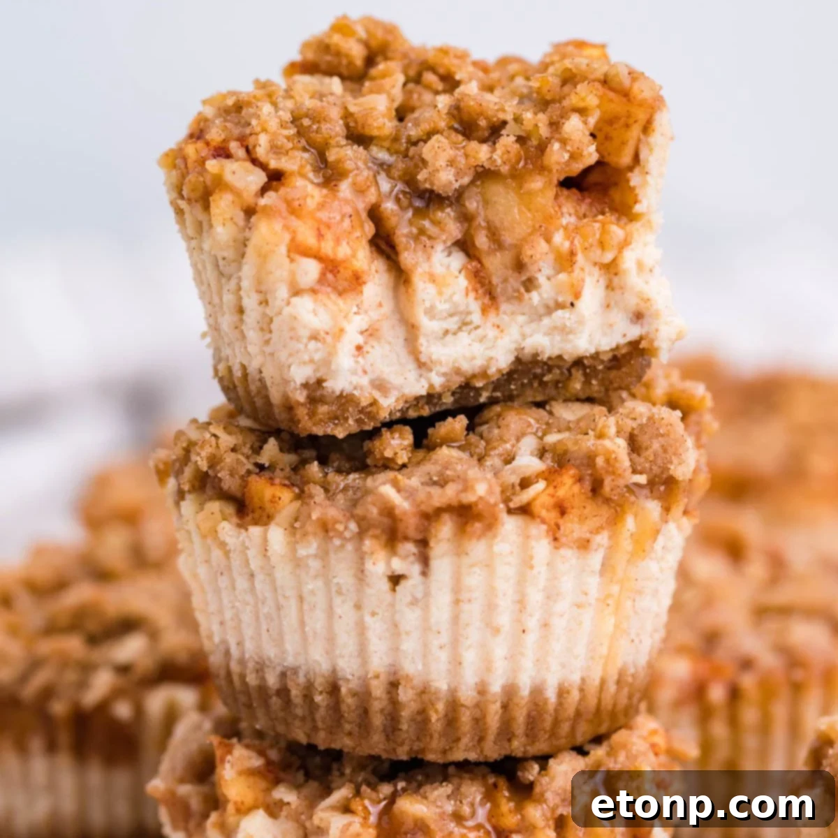 Mini Apple Crisp Cheesecakes stacked on top of one another on table with more spread out behind it on table 