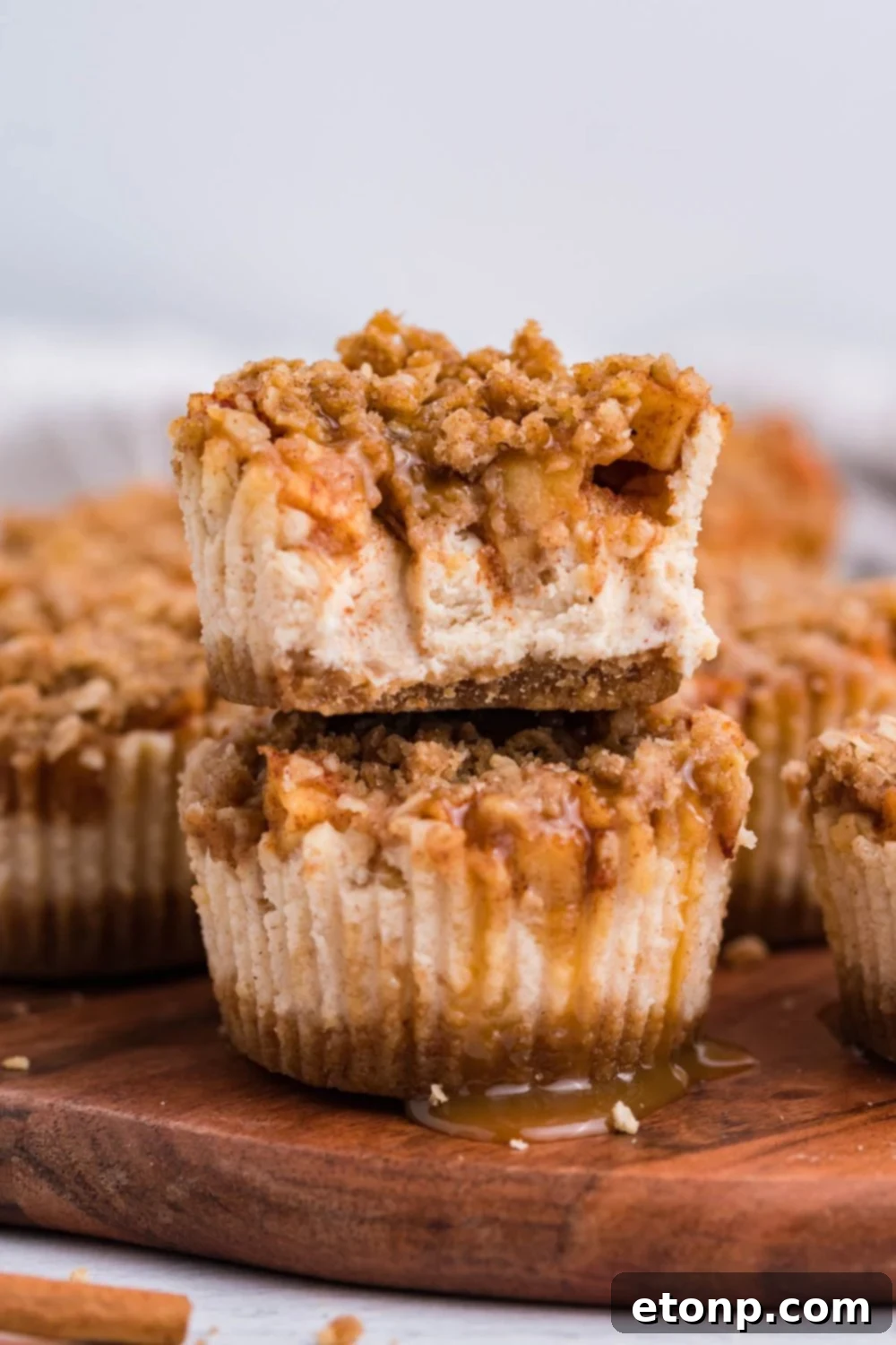 cutting board on marble table with two Apple Crisp Cheesecake Bites stacked on top of one another, and top cheesecake has bite taken out of it. Then around the board are more cheesecakes. 