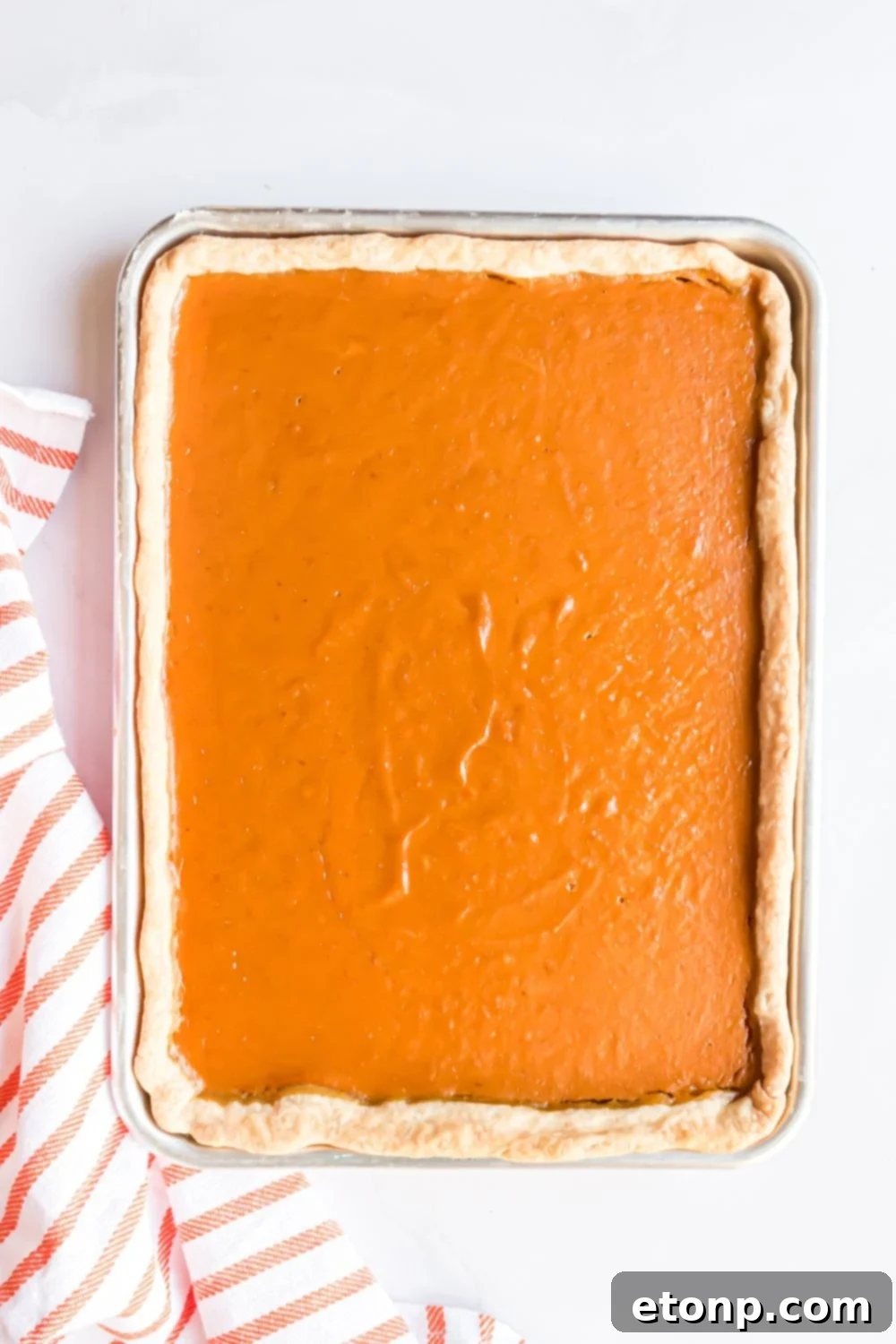 Effortless 4-Ingredient Sheet Pan Pumpkin Pie 11 baked Sheet Pan Pumpkin Pie sitting on a white table with a red and white striped towel to the side