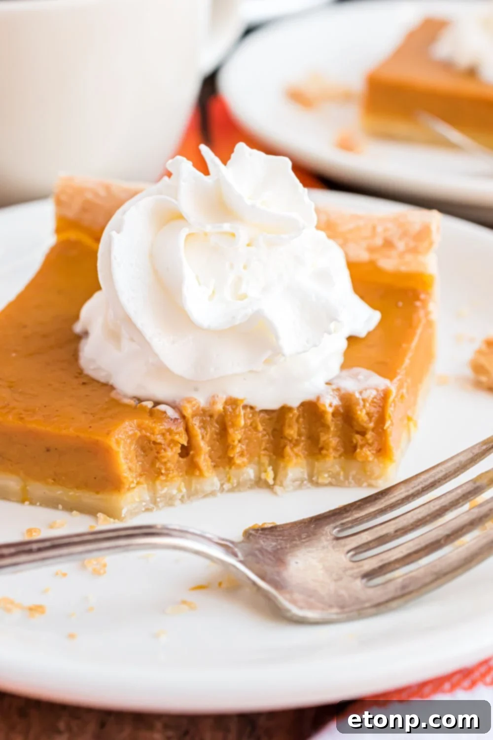 Effortless 4-Ingredient Sheet Pan Pumpkin Pie 14 Homemade pumpkin pie squares sitting on white plates with one with a bite taken out with fork marks in the pie with a fork sitting in front of slice of pie on wood table